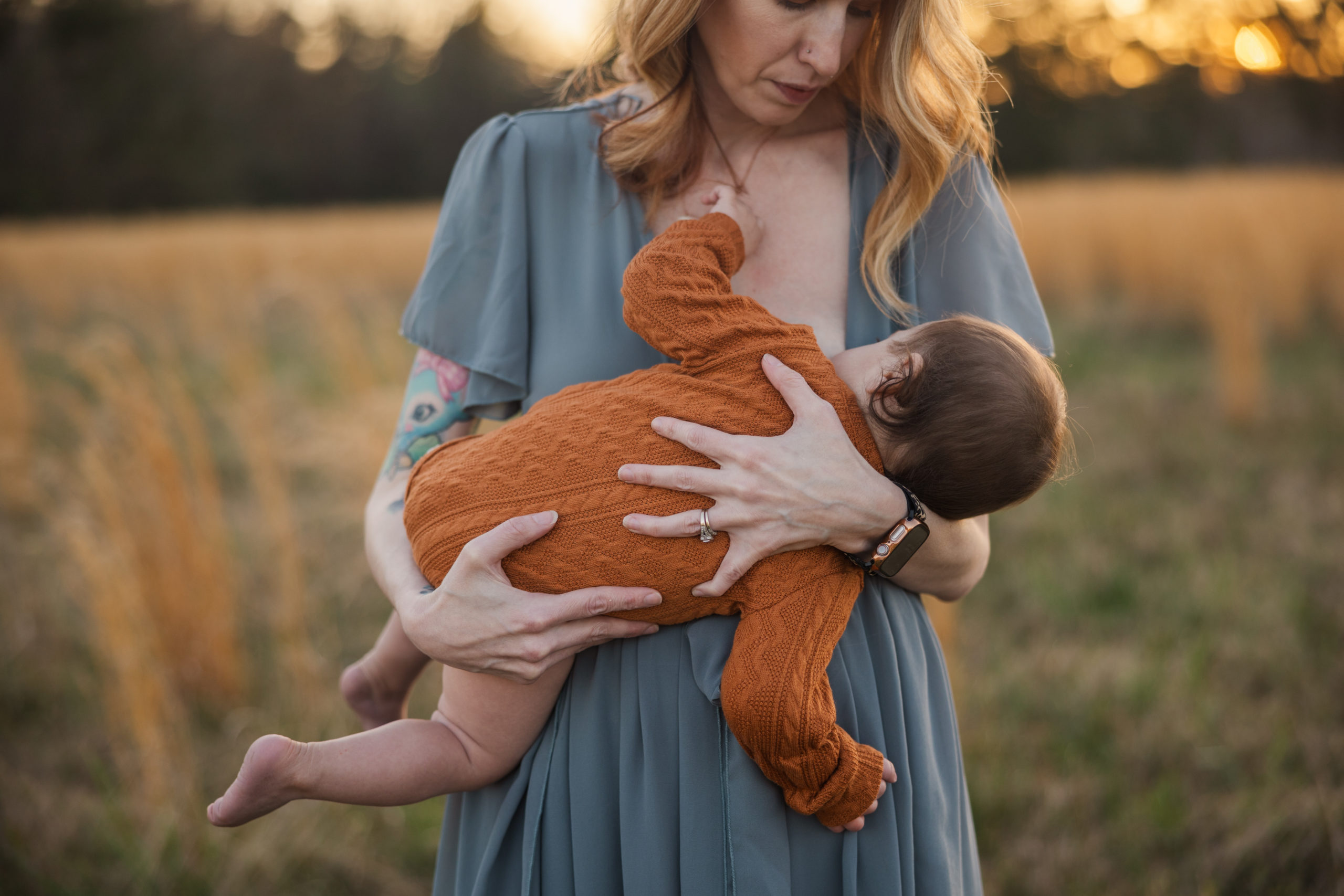 Mom breastfeeding 8 month old boy at milestone session. Mom is wearing a Baltic Born Gown. Session took place in an open field at sunset in Grovetown, Georgia.