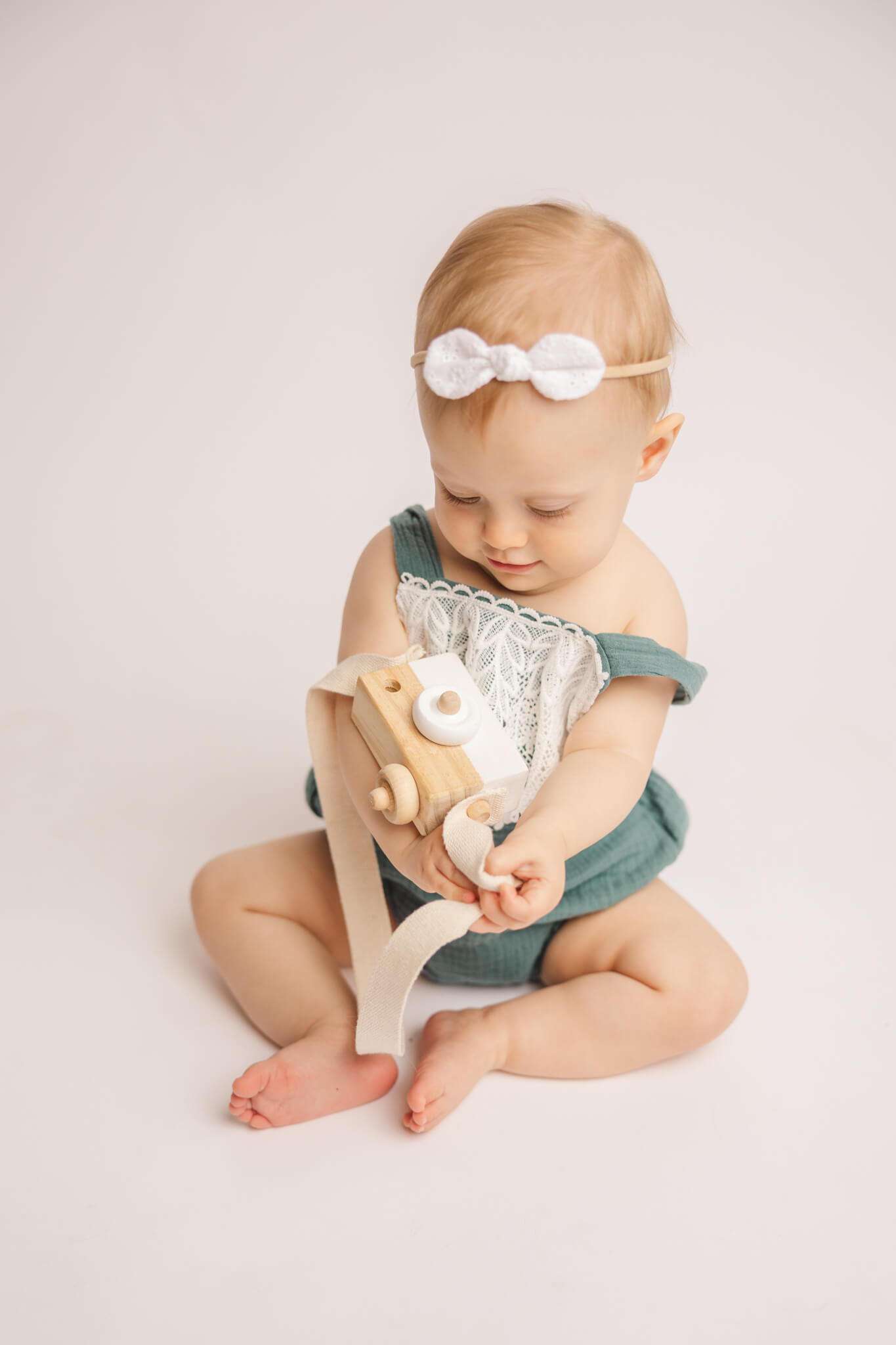 One year old sweet girl playing with a wooden camera during her cake smash session