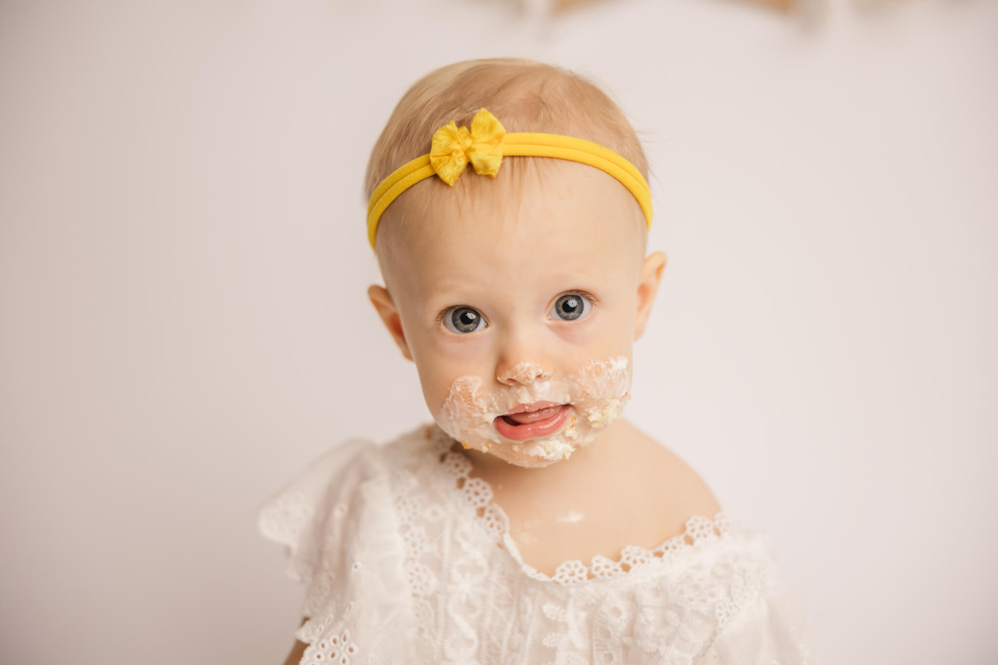 One year old baby girl smiling with her face covered in cake during her session.