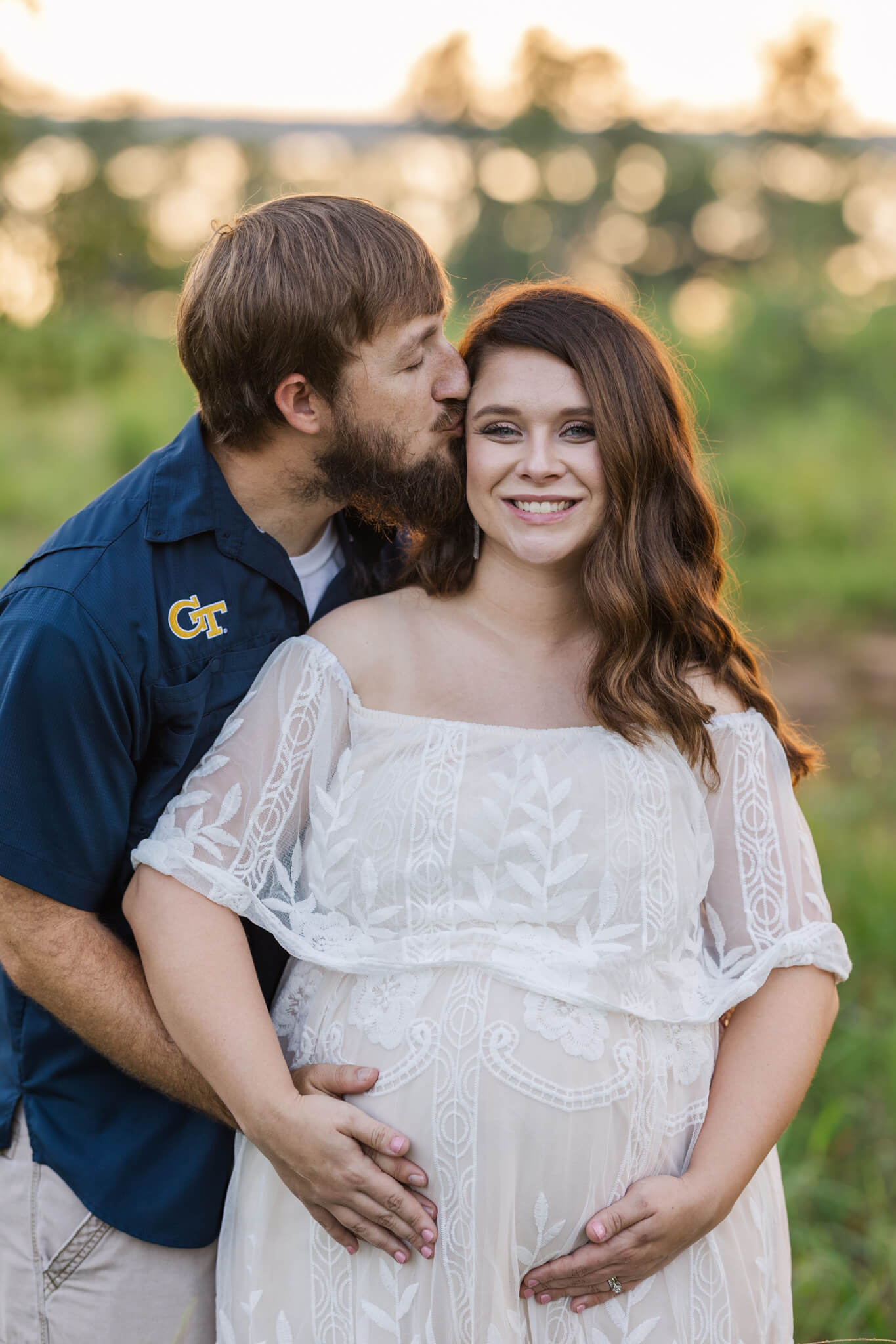Dad is kissing mom on the temple during their maternity session in an open field at golden hour. birthing center augusta ga