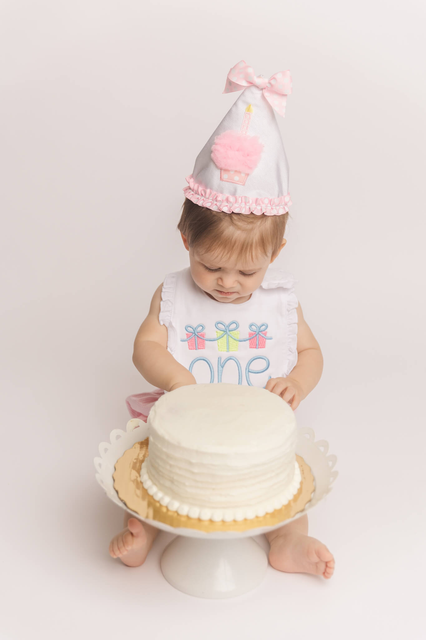 one year old showing off her new party had at bib during her cake smash session