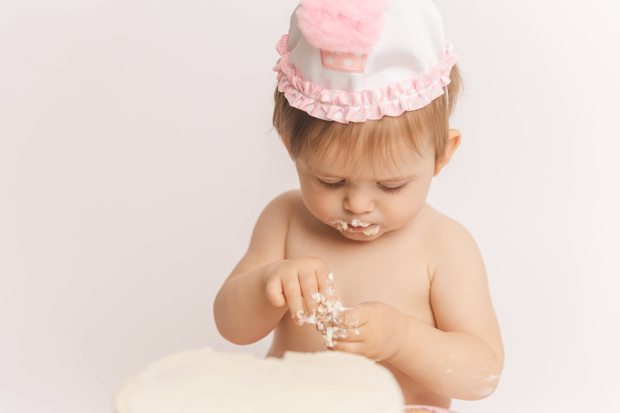 Close up of baby girl focused on the cake on her hands during her cake smash session in Augusta, GA. Baby Stores Augusta GA