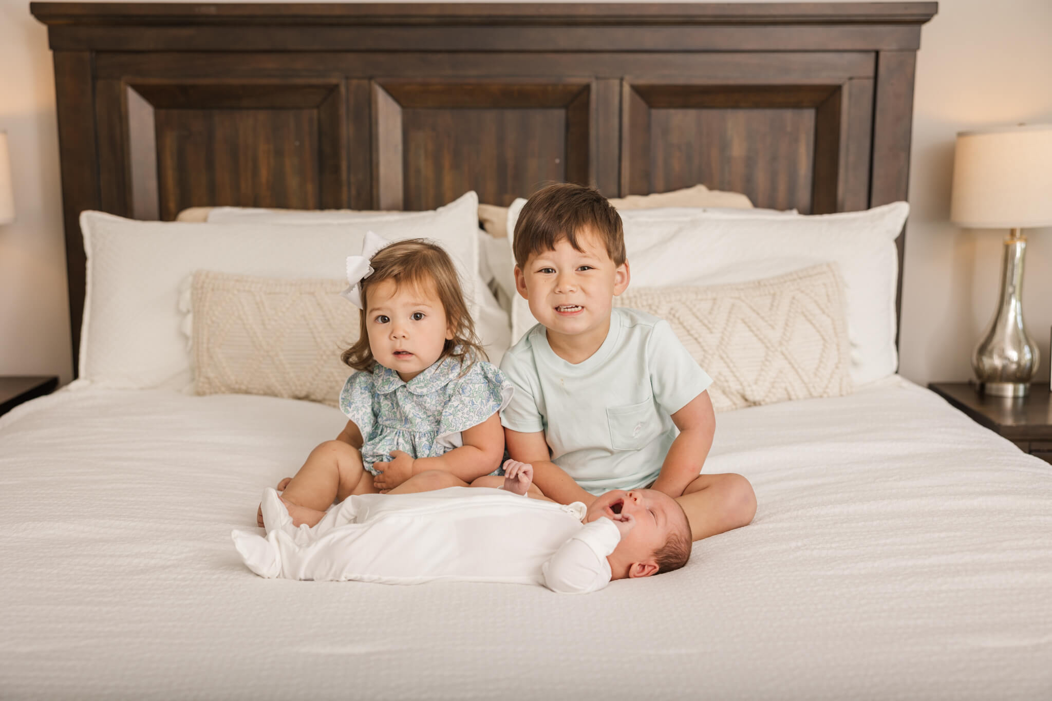Big brother and sister sitting with baby brother on the bed during their newborn session in their home by Molly Berry. The Swank Company