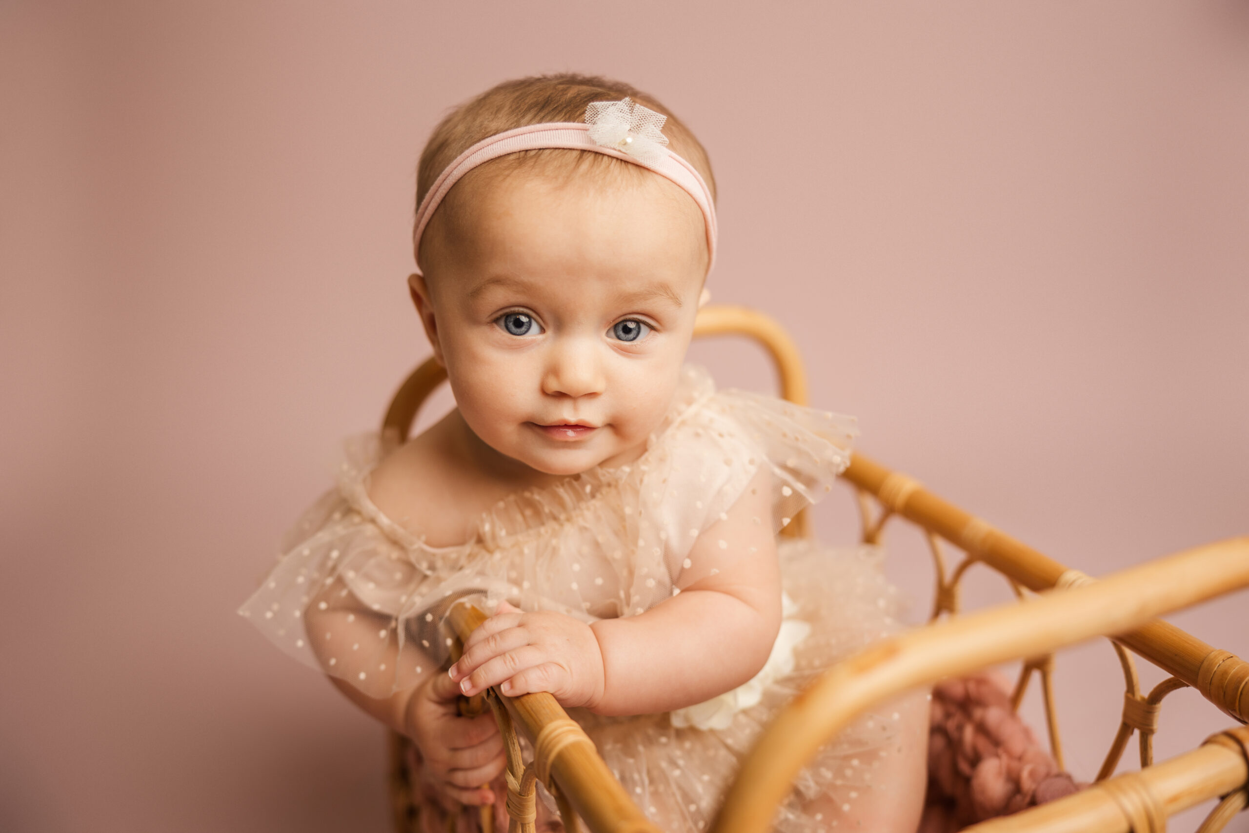 6 month old baby girl sitting in a wicker basket during her milestone studio session with molly berry.

