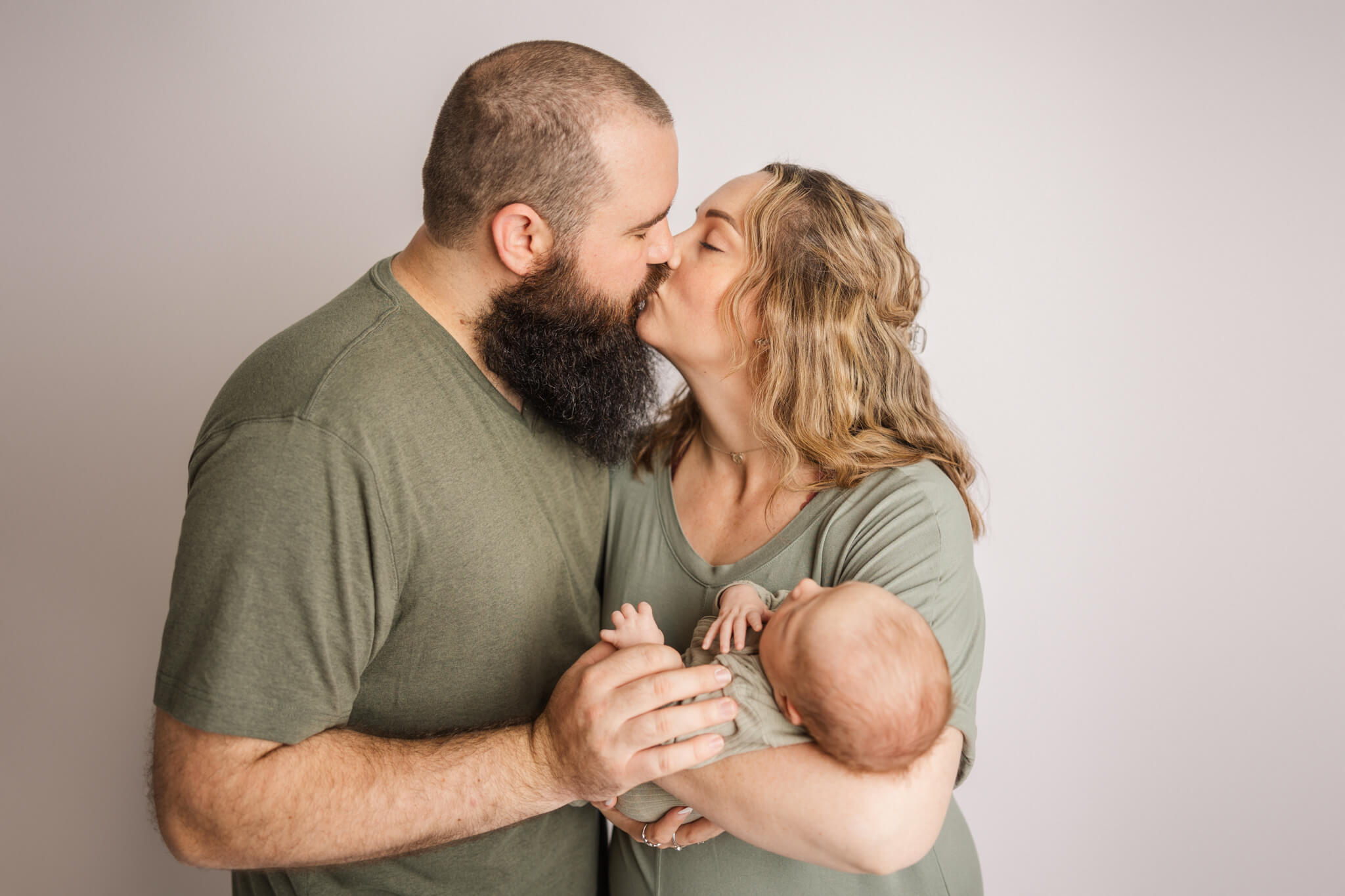 new mom and dad dressed in green kissing while holding their newborn
