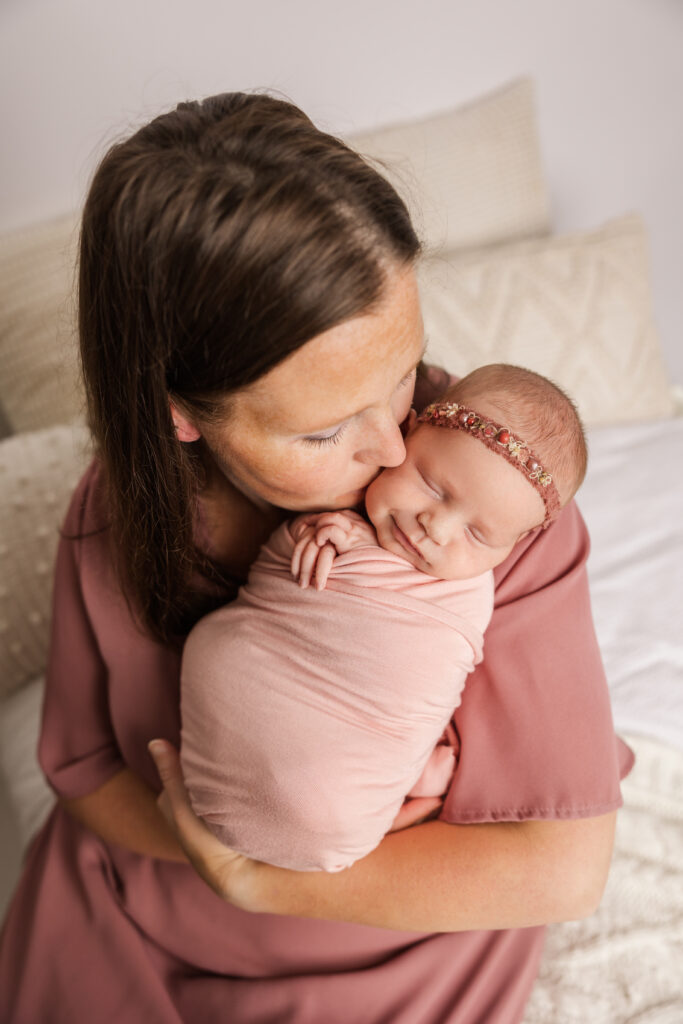 Newborn baby girl and mom captured a sweet moment during their newborn session. Mom is wearing a pink gown from Pink Blush.
