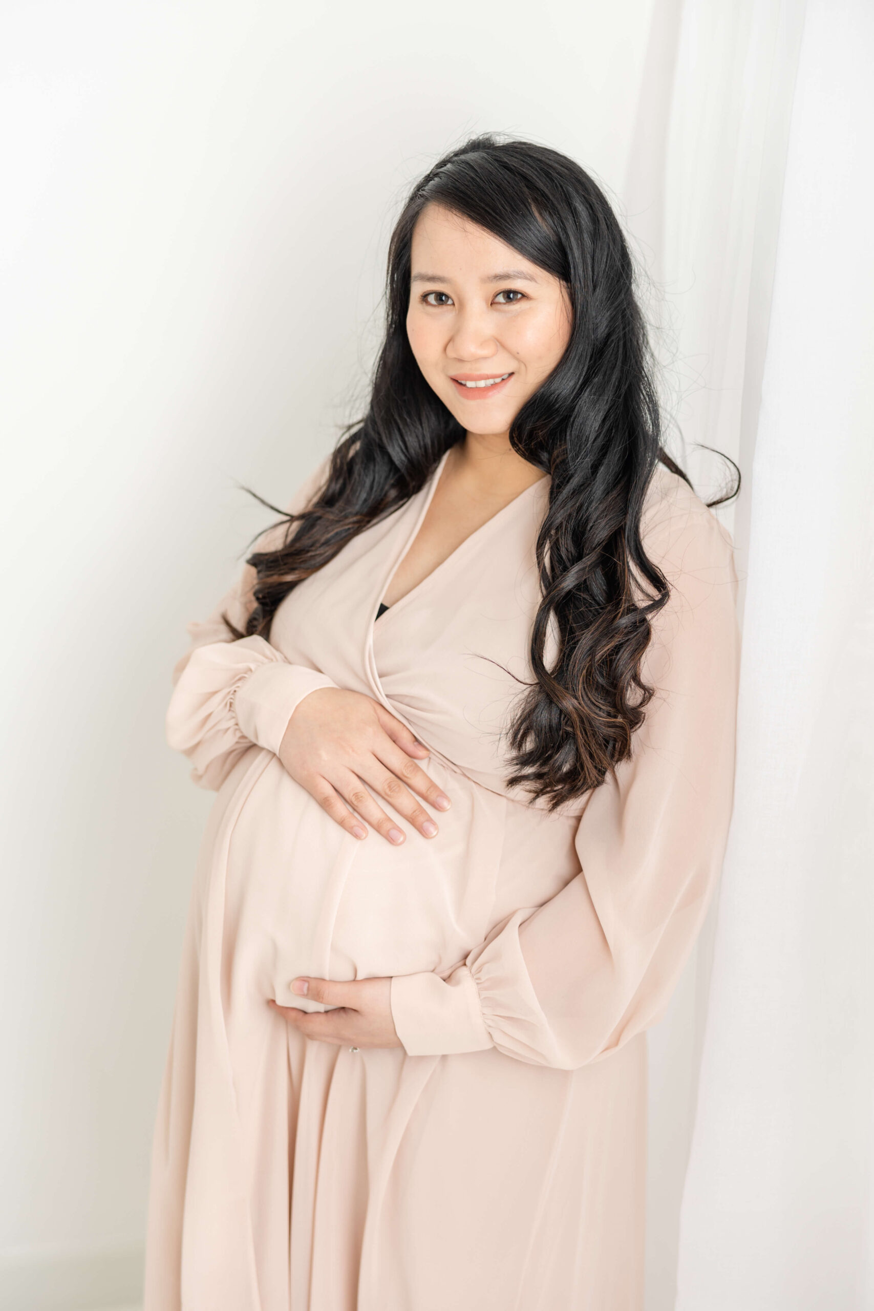 Soon to be mom in light pink, long sleeve dress shows her baby bump.