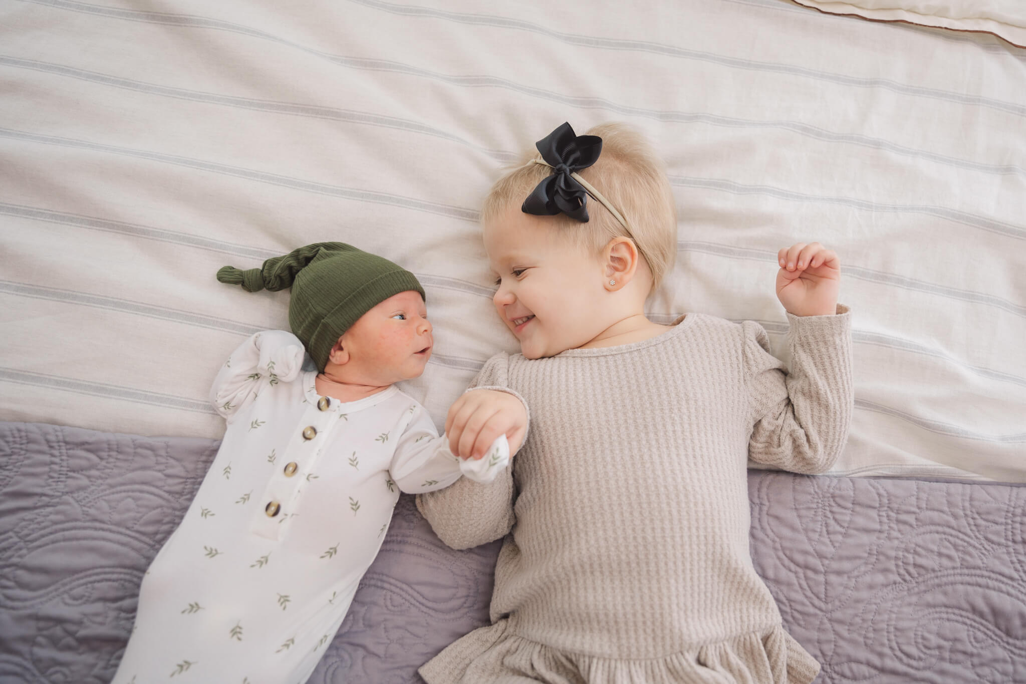 newborn baby in white onesie and green hat laying hand in hand with his sister Augusta Care Pregnancy Center