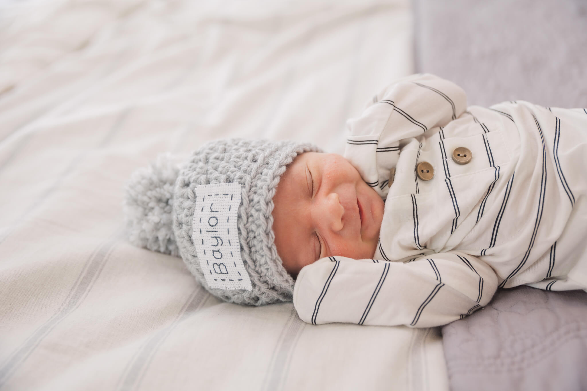 newborn baby in grey hat and striped onesie sleeping on a bed Augusta Care Pregnancy Center
