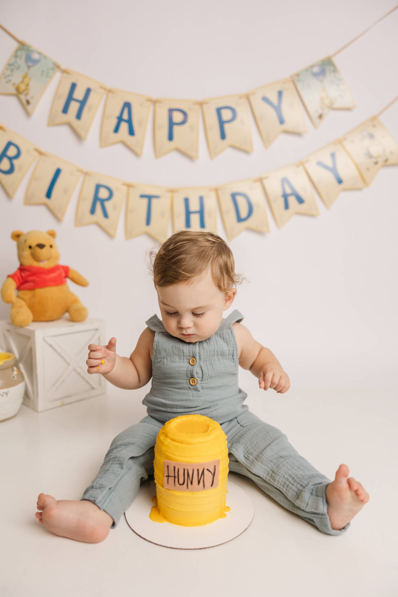 One year old enjoying his winnie the pooh themed cake smash session in the studio of molly berry photography.