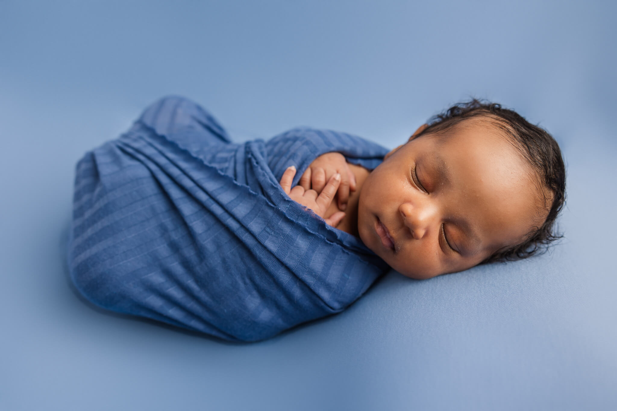 Newborn baby boy wrapped in blue swaddle during recent studio newborn session. Magnolia Chiropractic