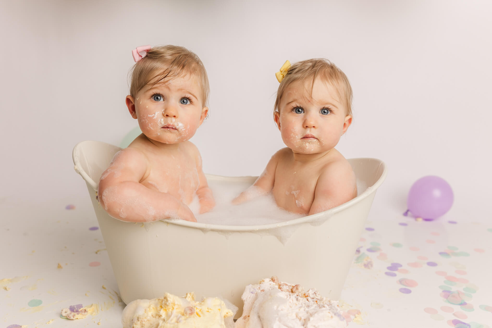 twin one year old girls sitting in a bathtub