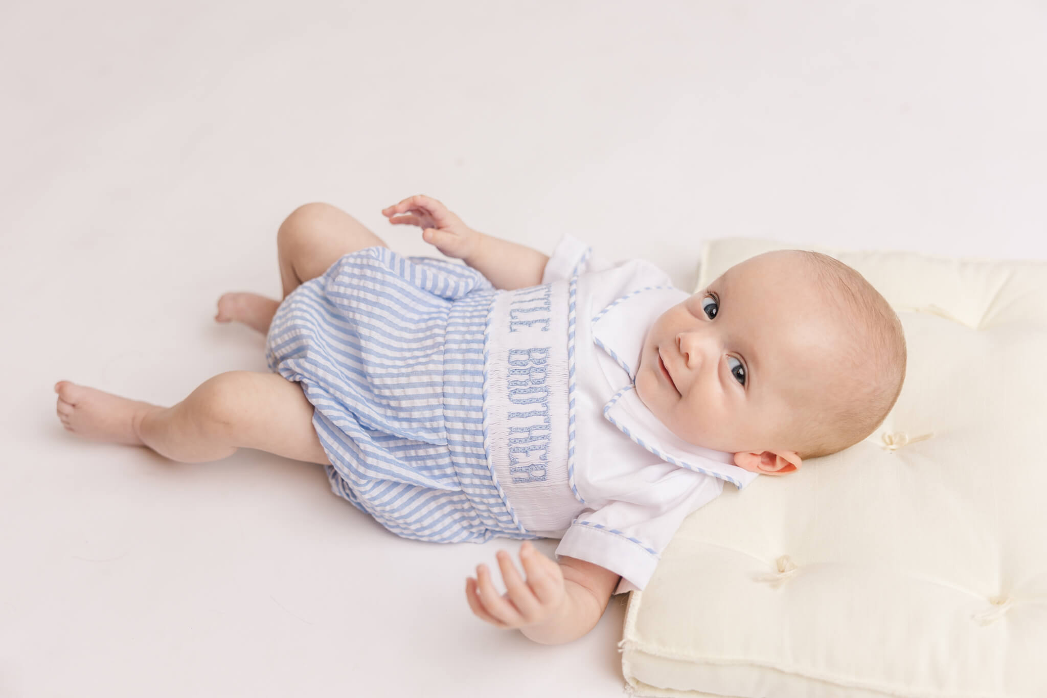 little boy in white and blue laying on a pillow smiling