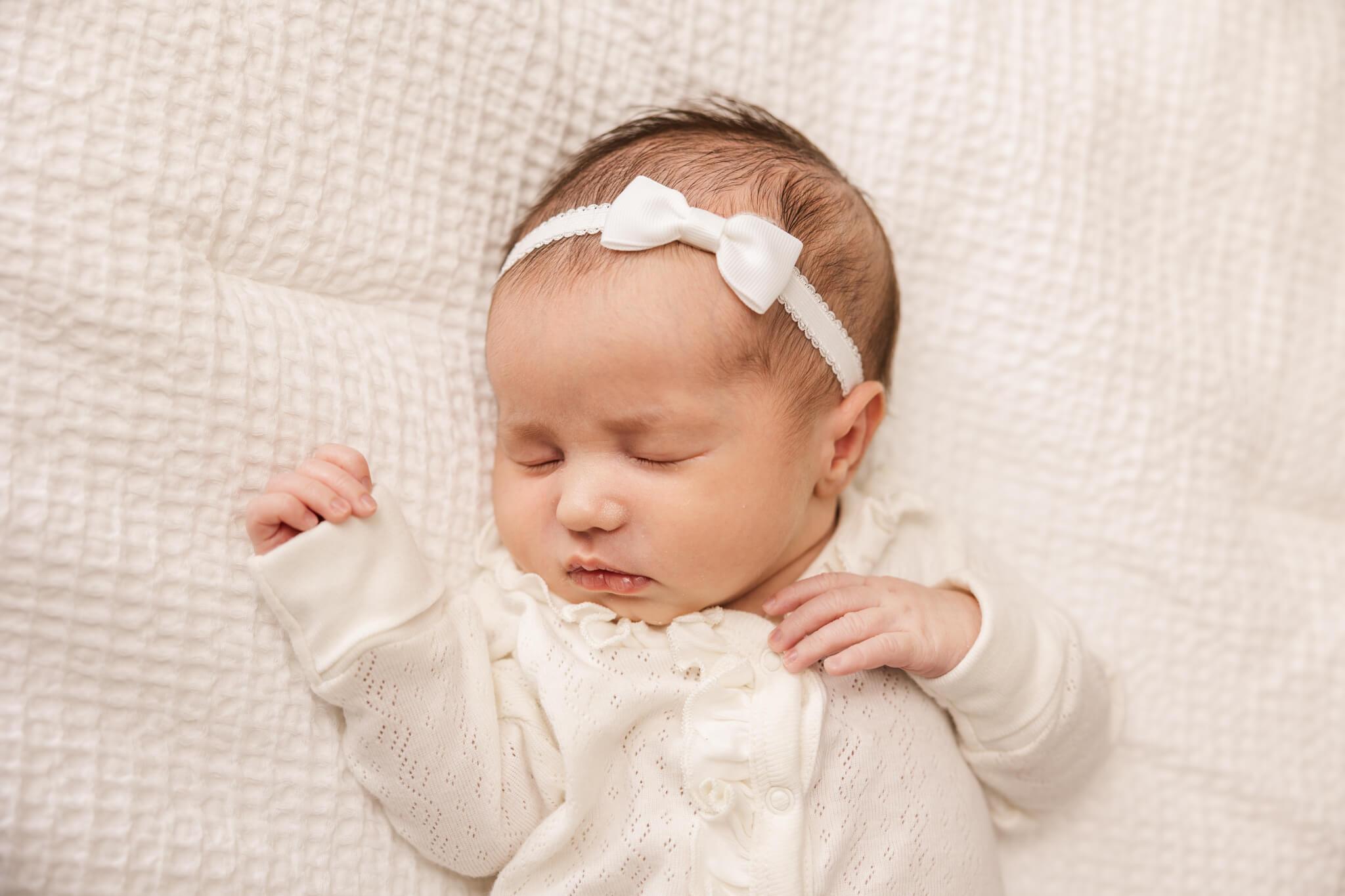 newborn baby girl in cream onesie and white headband sleeping Flack Family Chiropractic