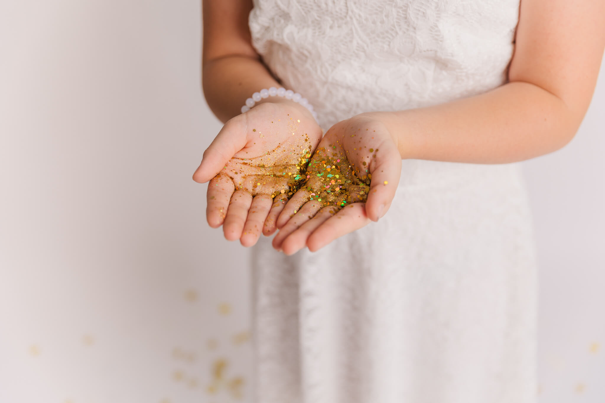 girl in white dress holding a handful of gold confetti