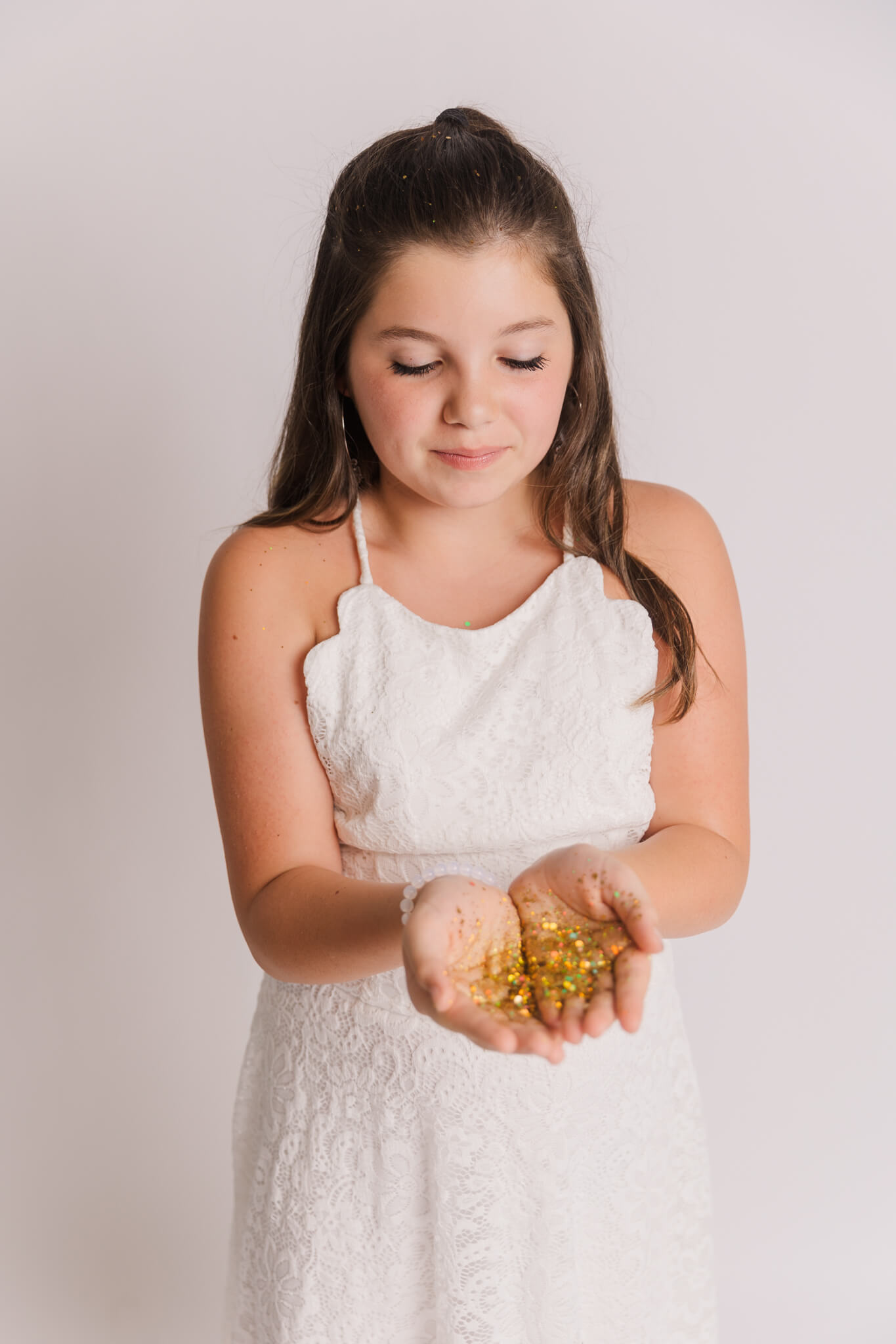 girl in white dress looking at her hands which are full of gold confetti Hayden Gymnastics