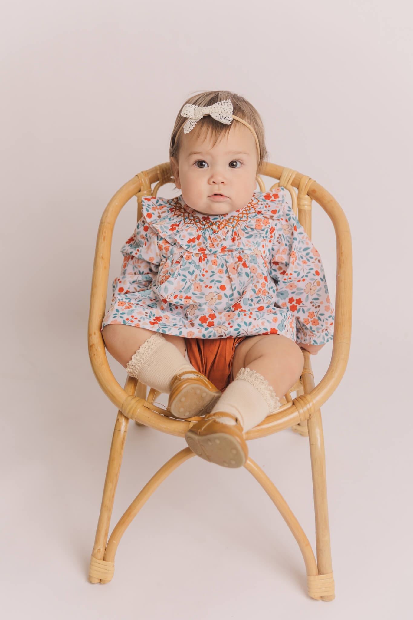 little girl in flowery dress sitting in a wicker chair
