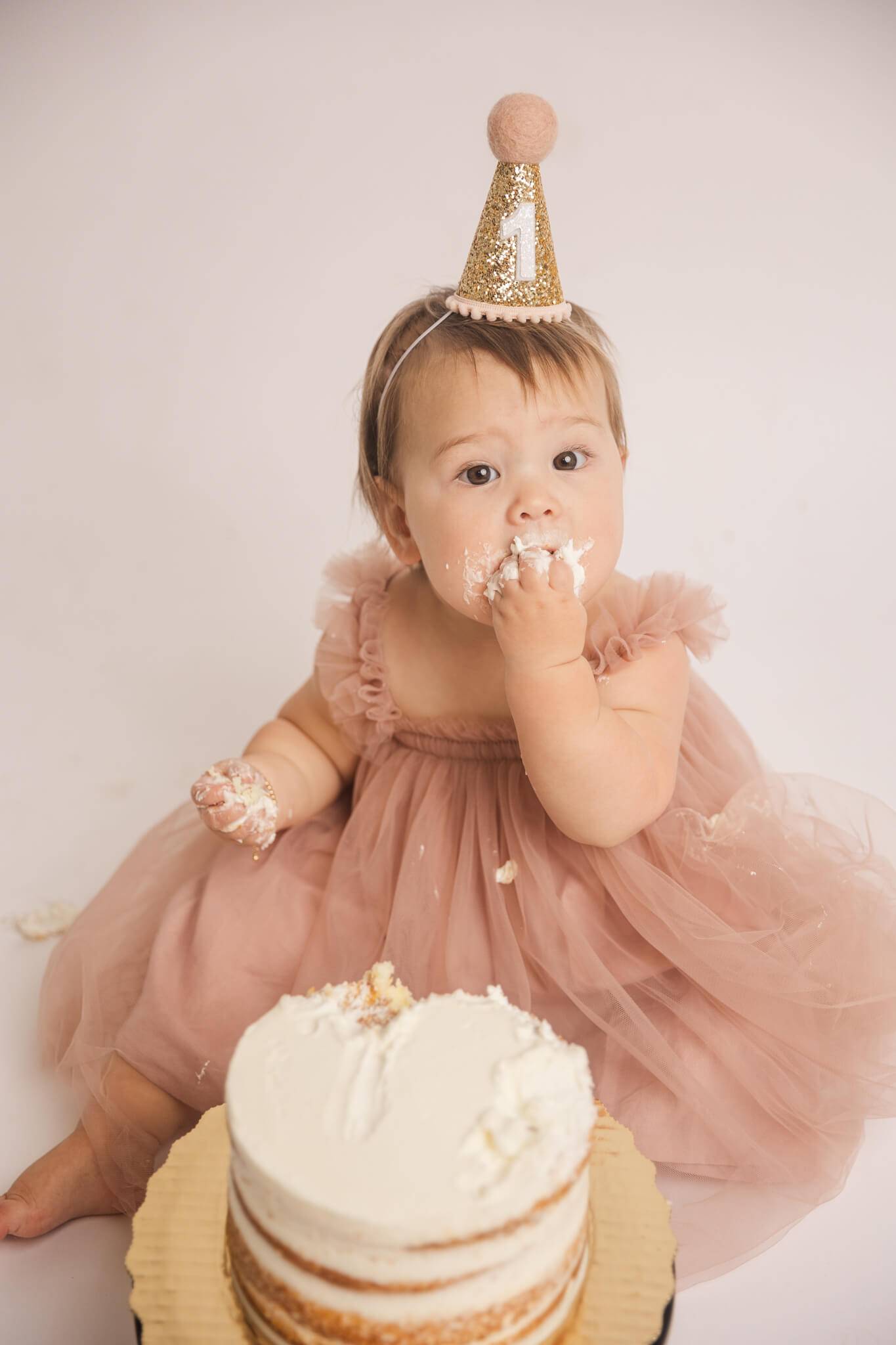 little girl in tulle pink dress and birthday hat eating cake