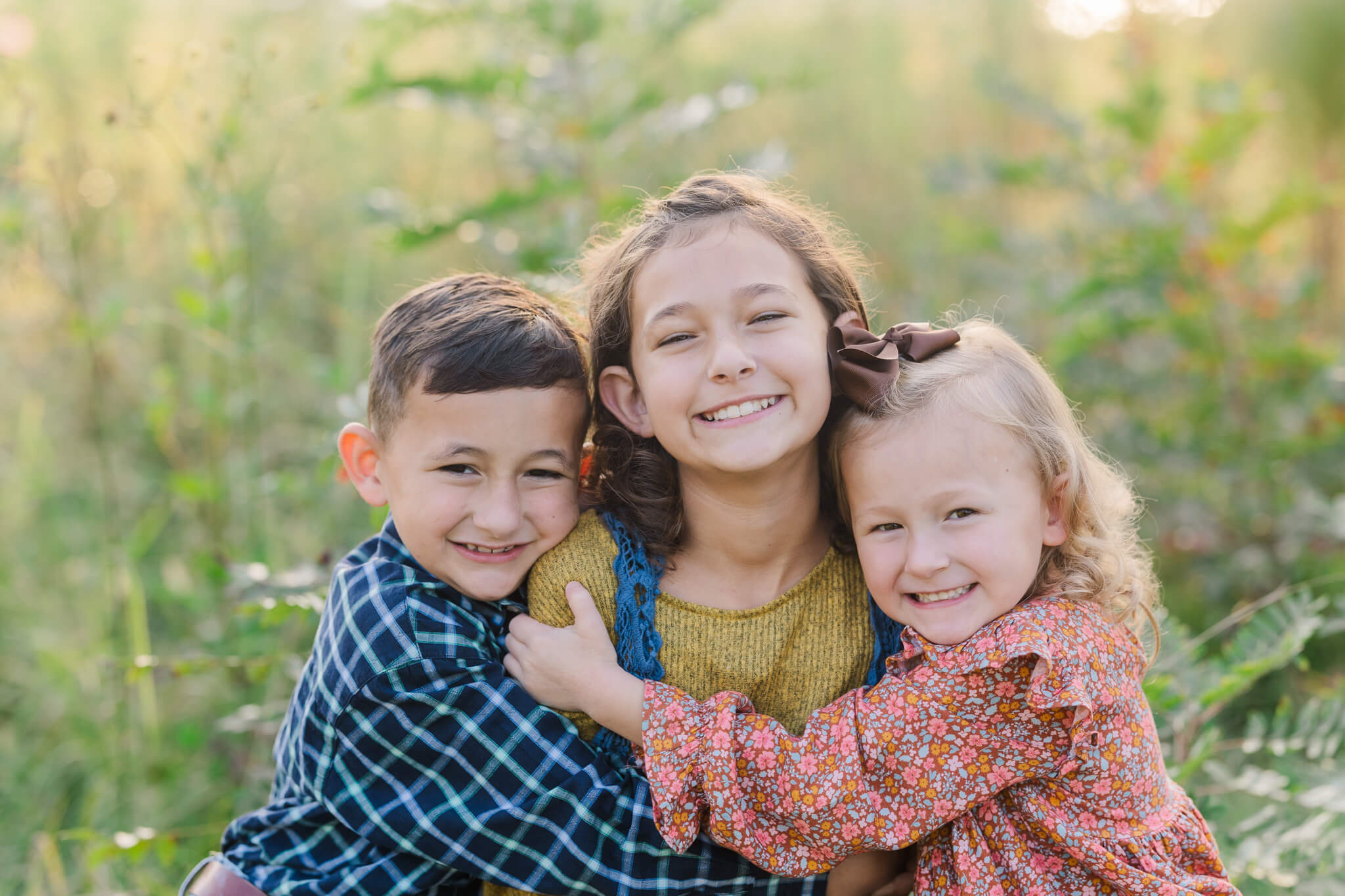 three siblings smiling widely for the camera and hugging in a field Pediatric Partners of Augusta