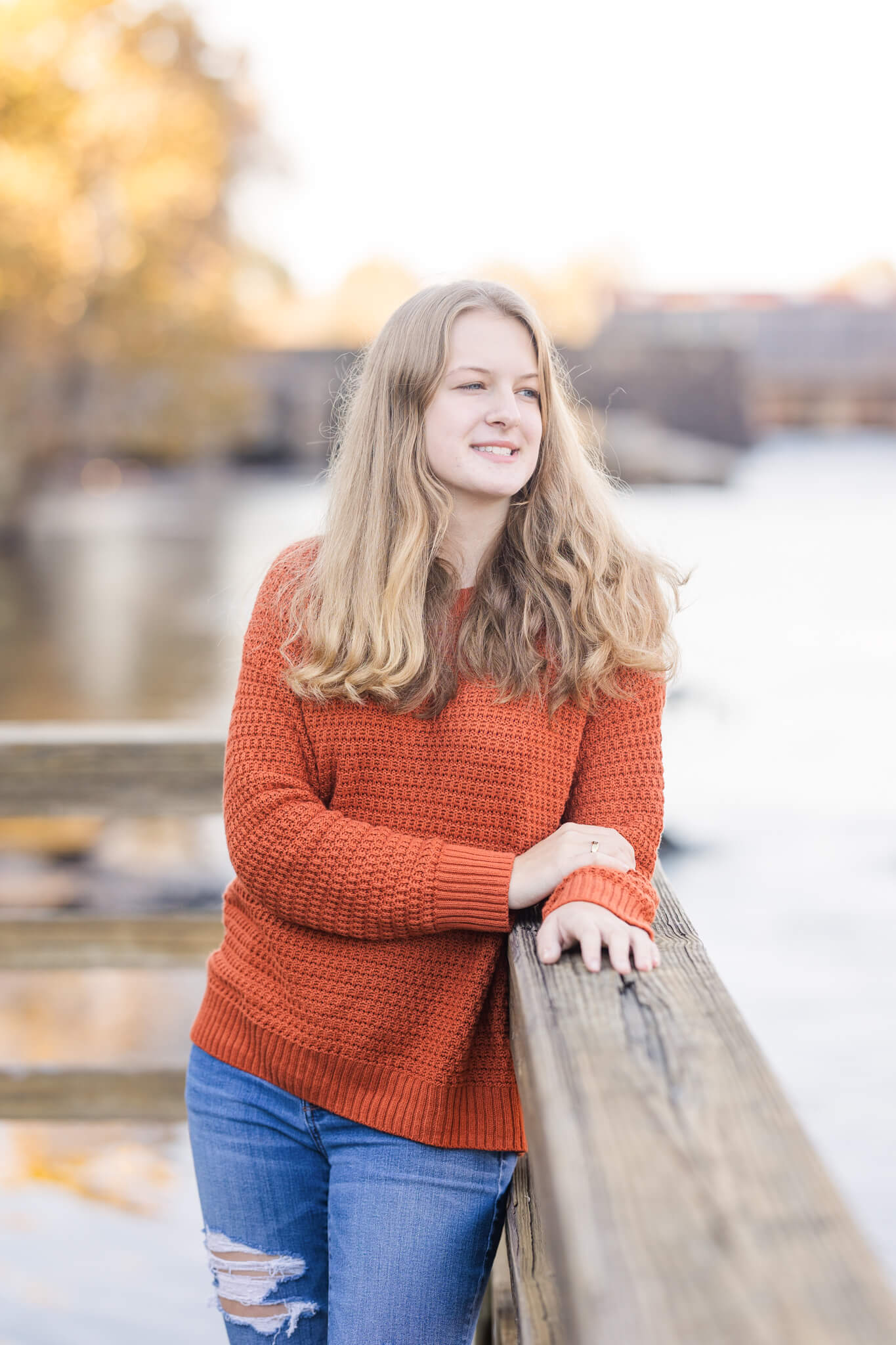 teenage girl in orange sweater leaning on a railing overlooking the water Uptown Cheapskate Evans GA