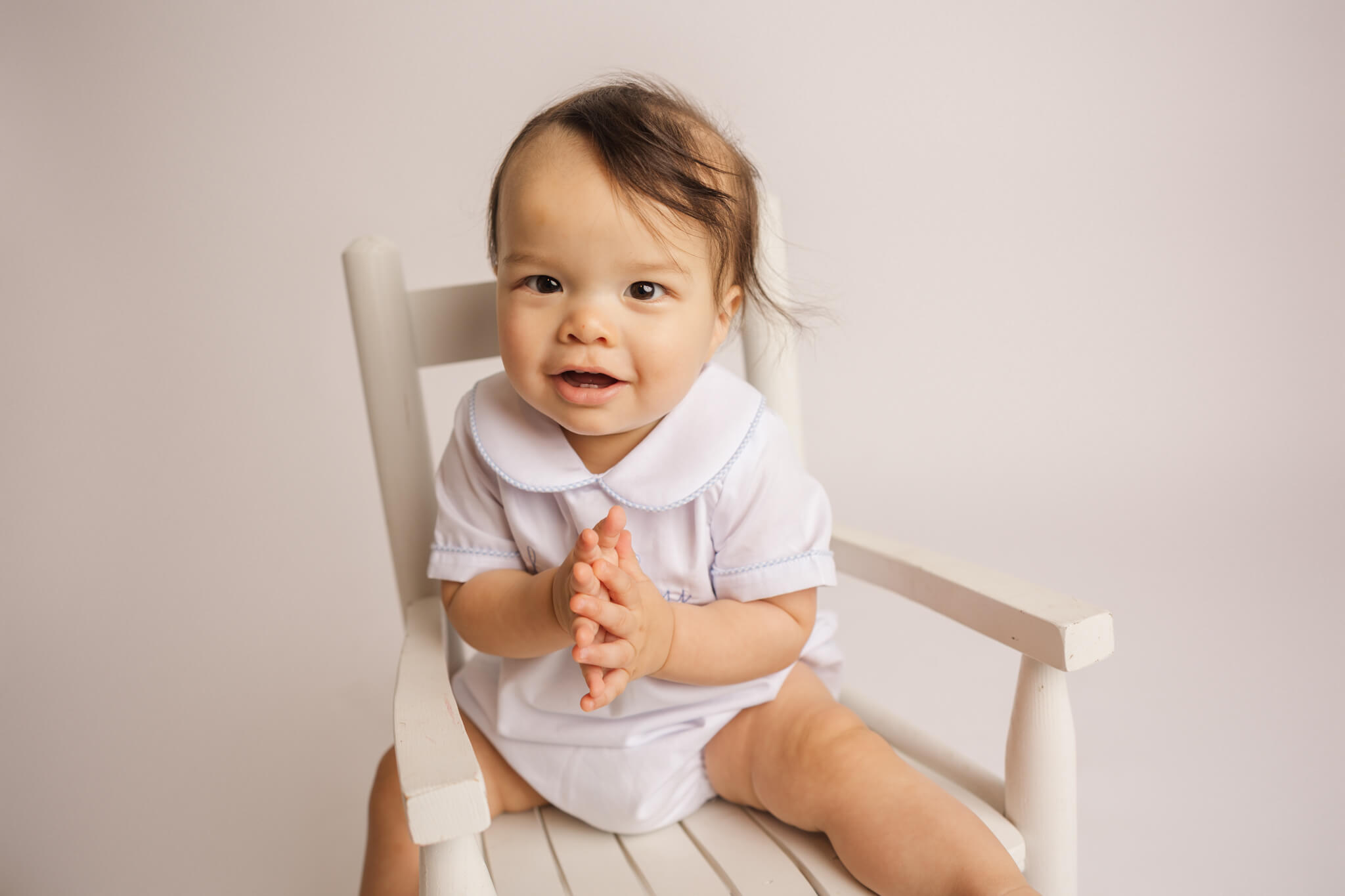 little boy in white onesie sitting in a rocking chair clapping his hands