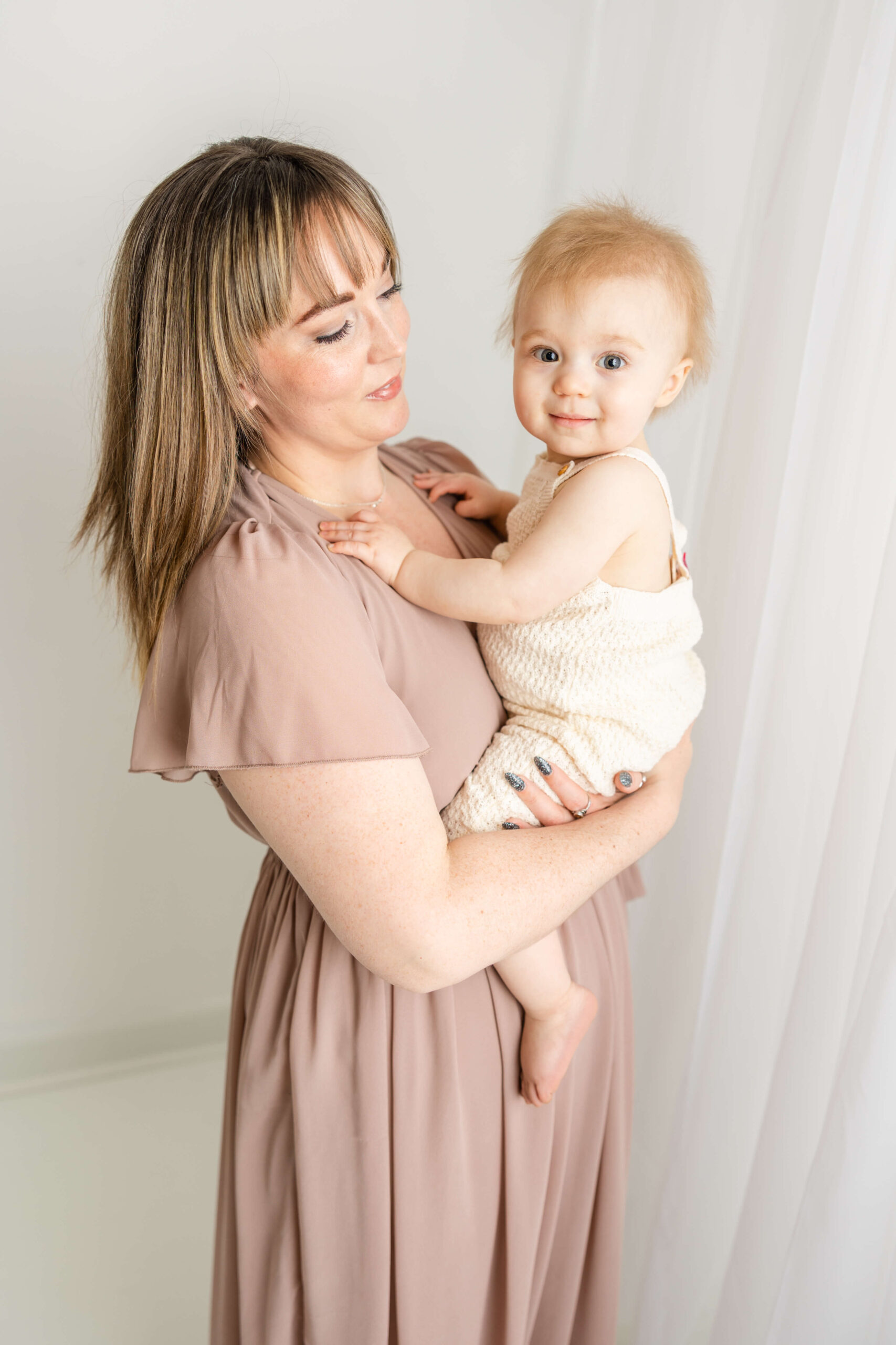 Captured mom, wearing a mauve gown while holding her baby girl in a white romper, both from client closet. 