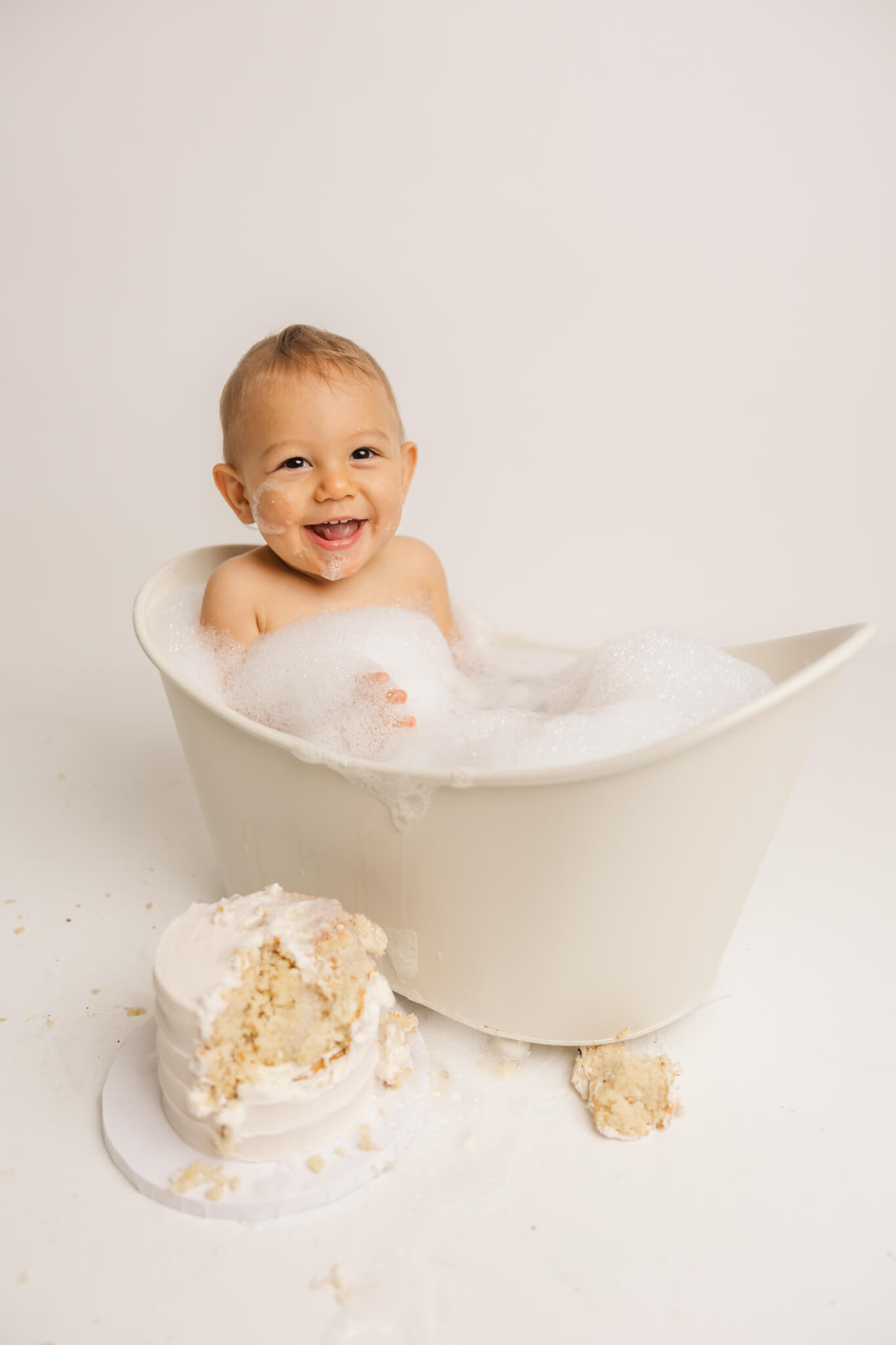 1 year old cleaning up in bathtub after cake smash session