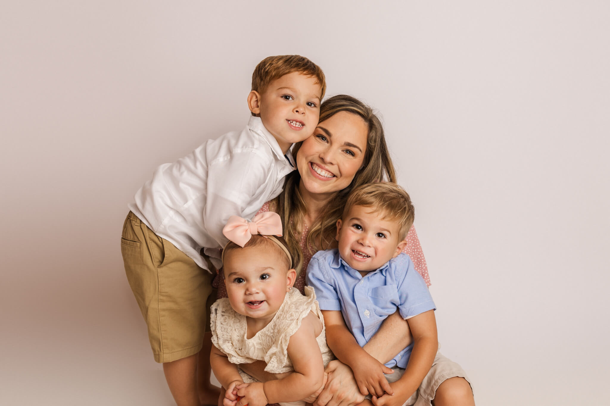 Family of four capturing a family photo in the studio during the youngest one year cake smash session. Mom and three children are wearing clothes from the client closet of molly berry photography.