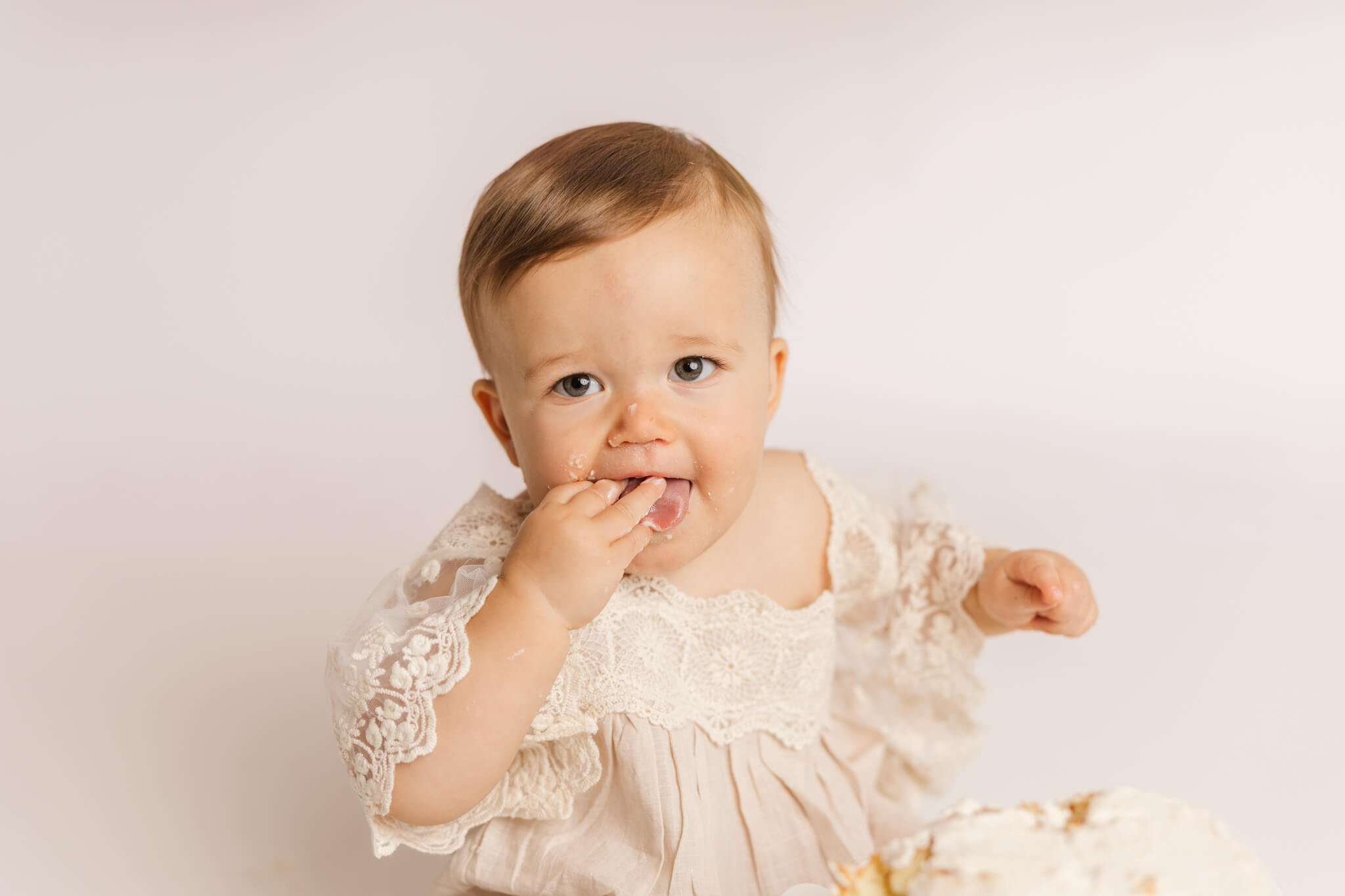 One year old girl in white lace dress at cake smash session.