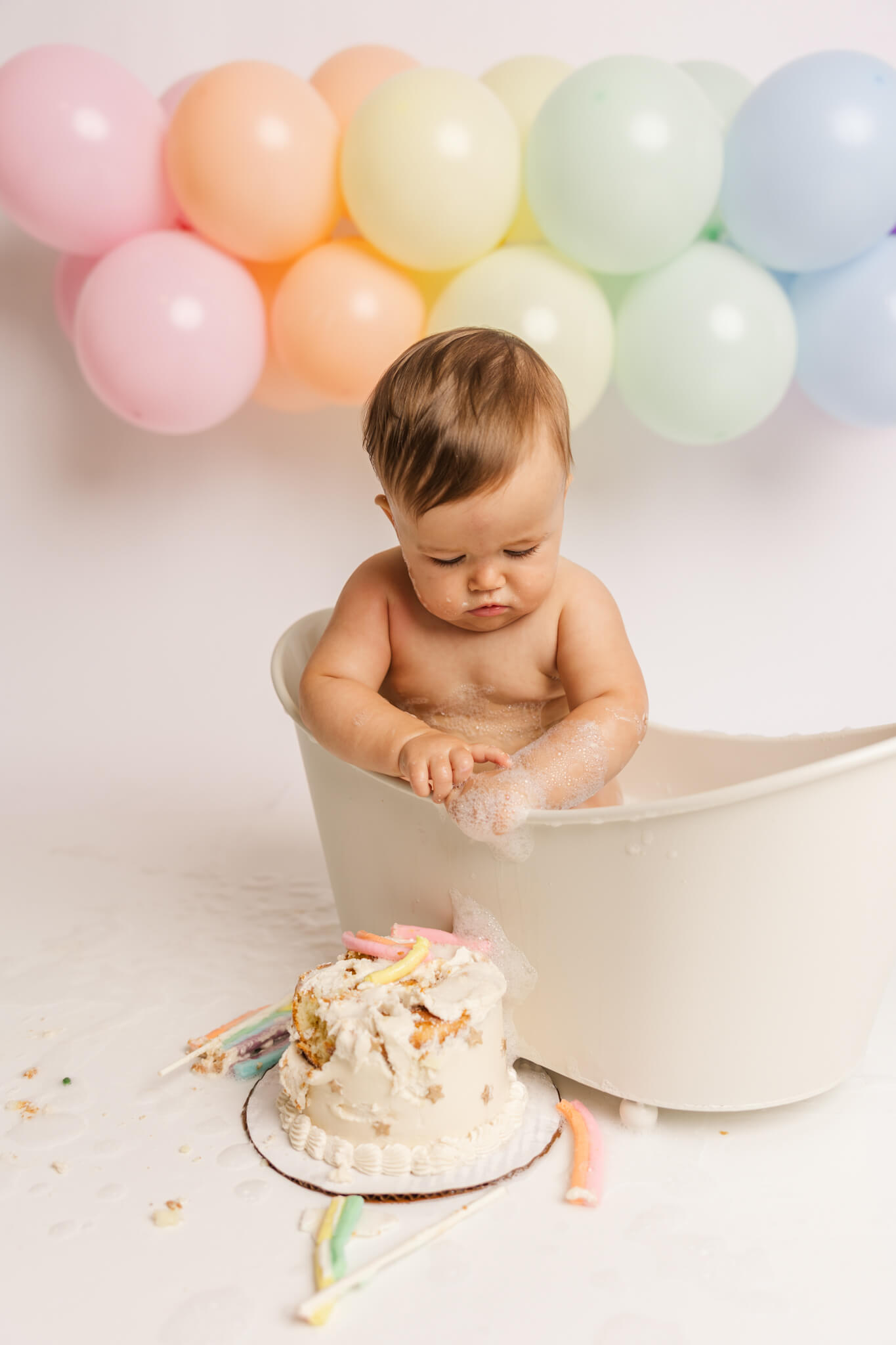 One year old girl getting cleaned up in bathtub after cake smash session.