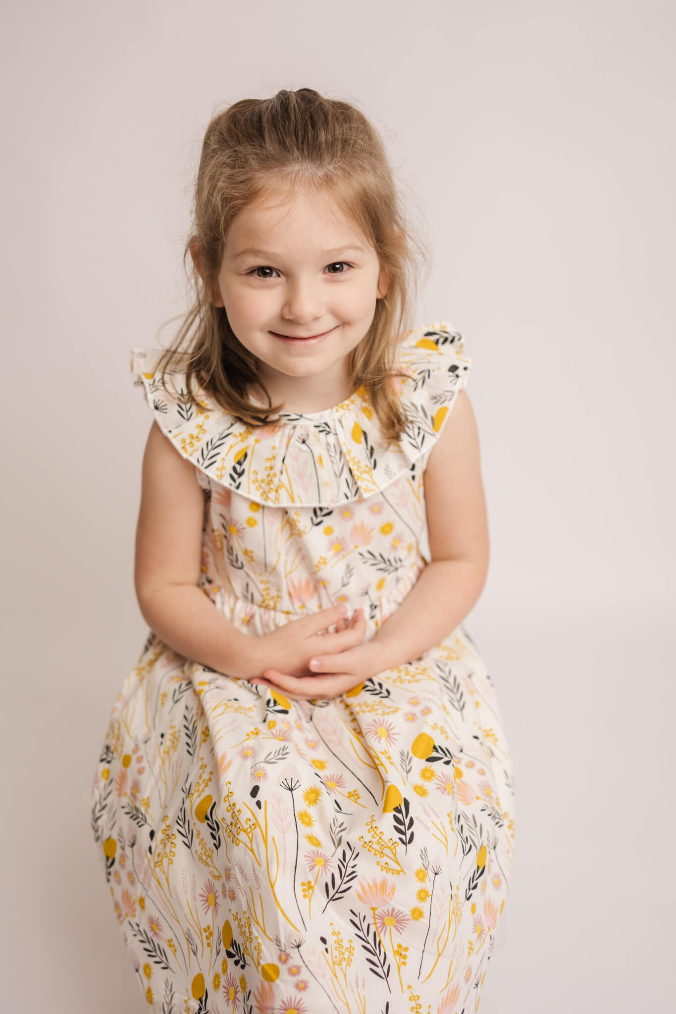 Sweet girl wearing yellow and pink dress during her milestone portraits in the studio with her siblings.