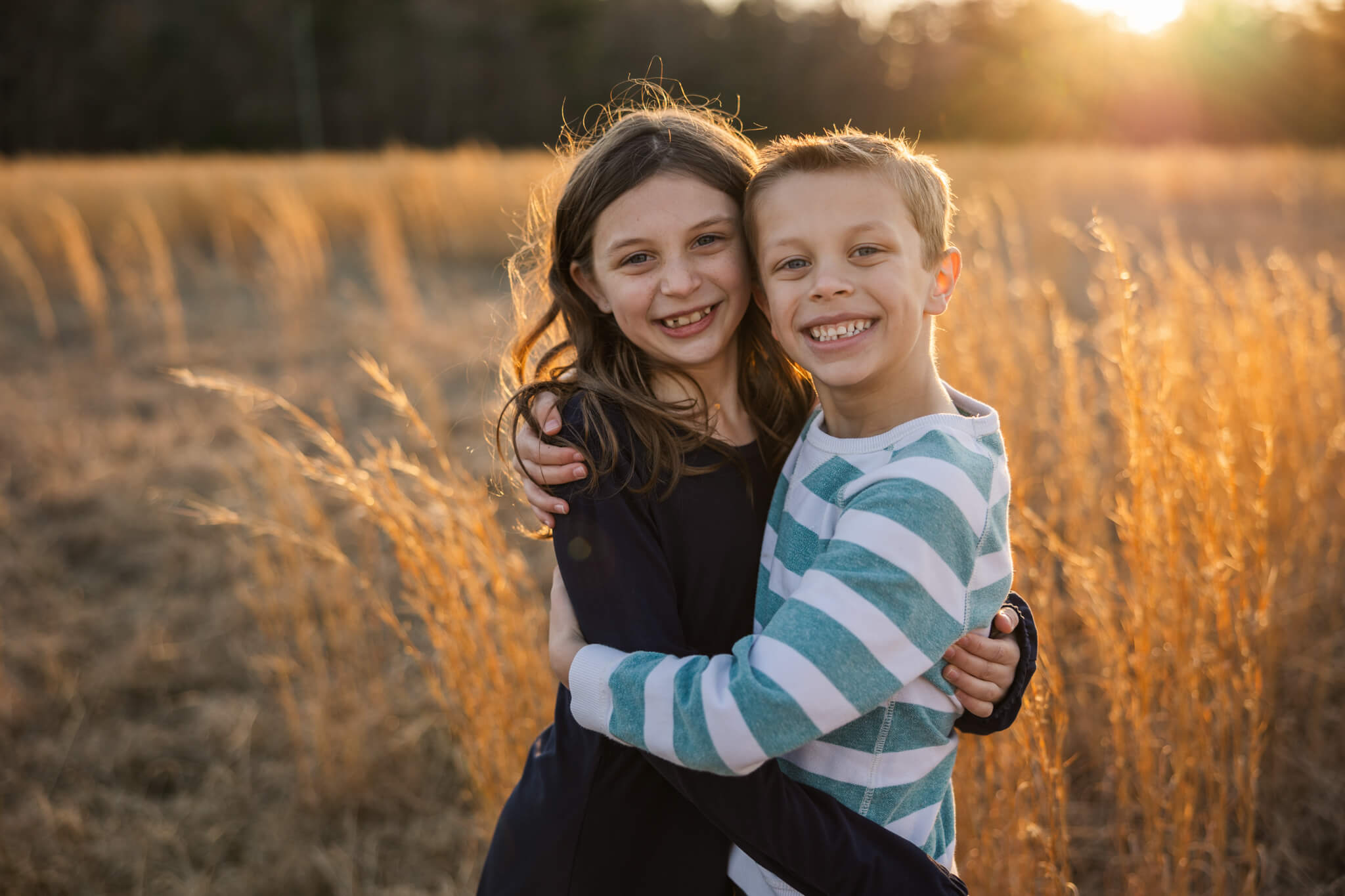 Siblings sharing a hug in the tall grass during a family session.