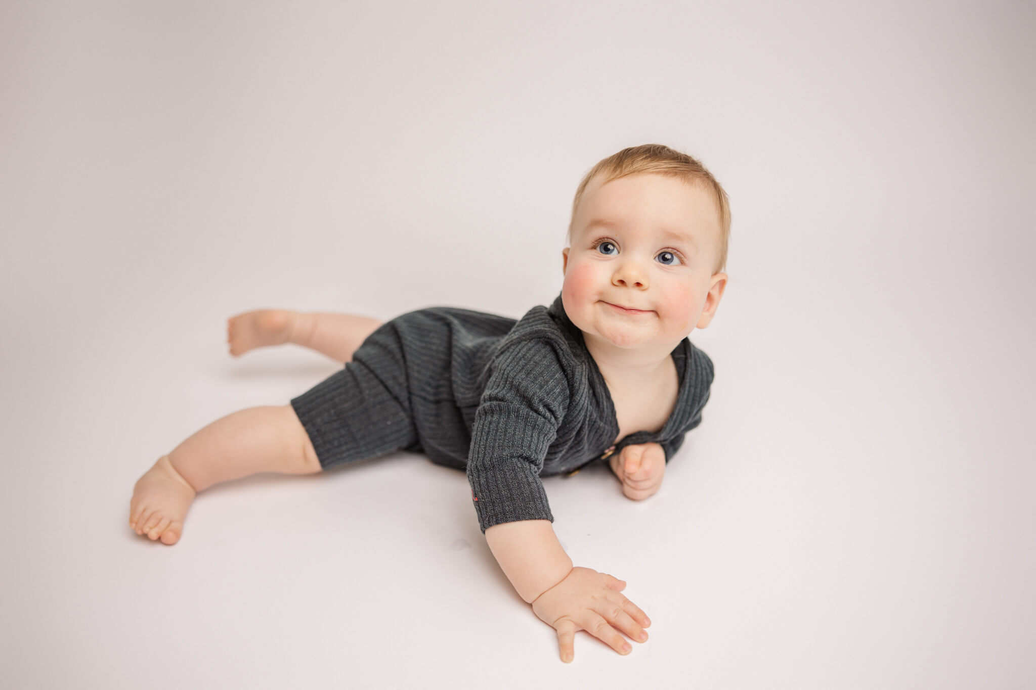 little boy smiling in a grey onesie while laying on the ground Pediatric and Prenatal Chiropractors in Augusta
