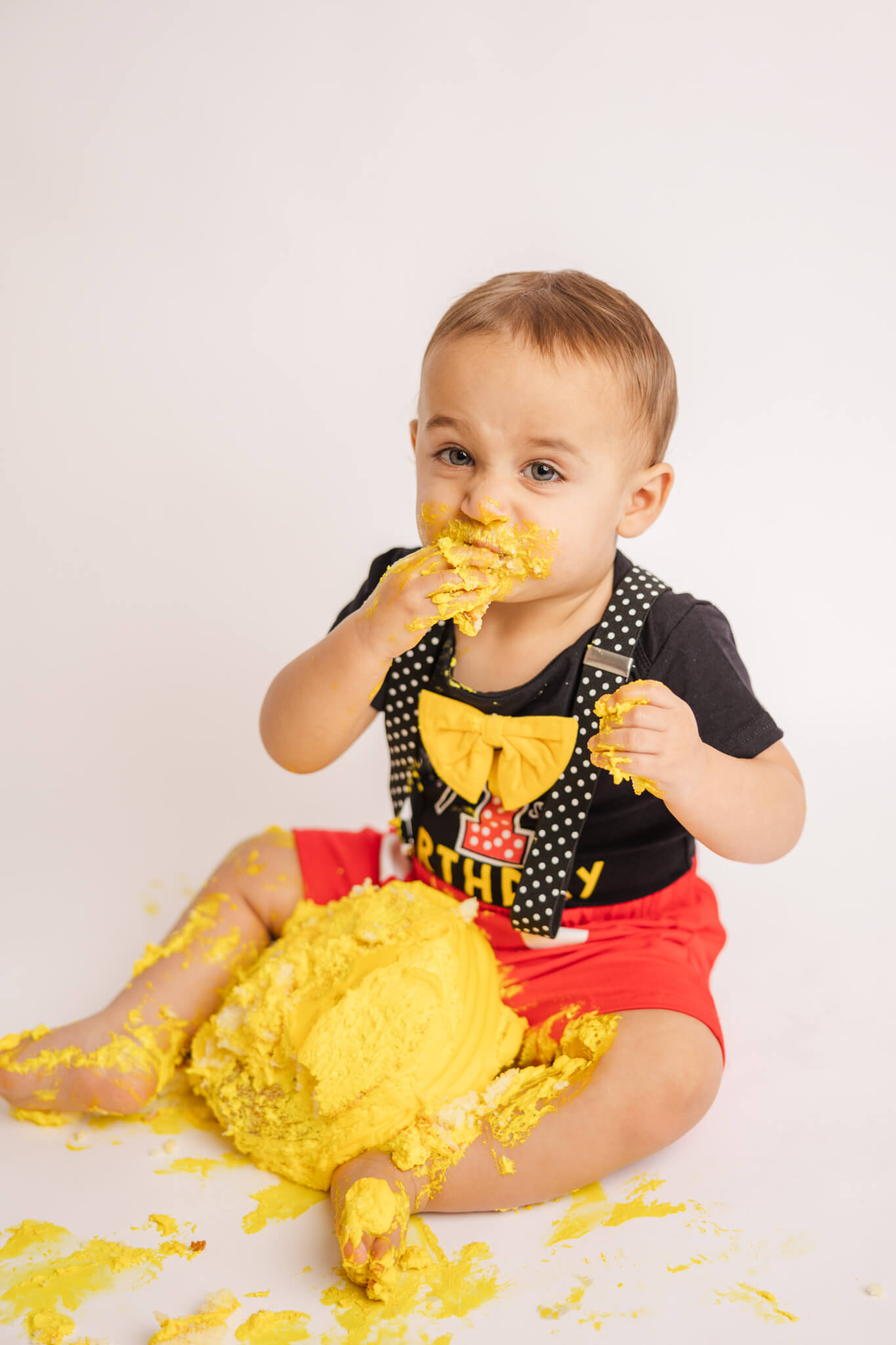 little boy in black and red eating his yellow birthday cake