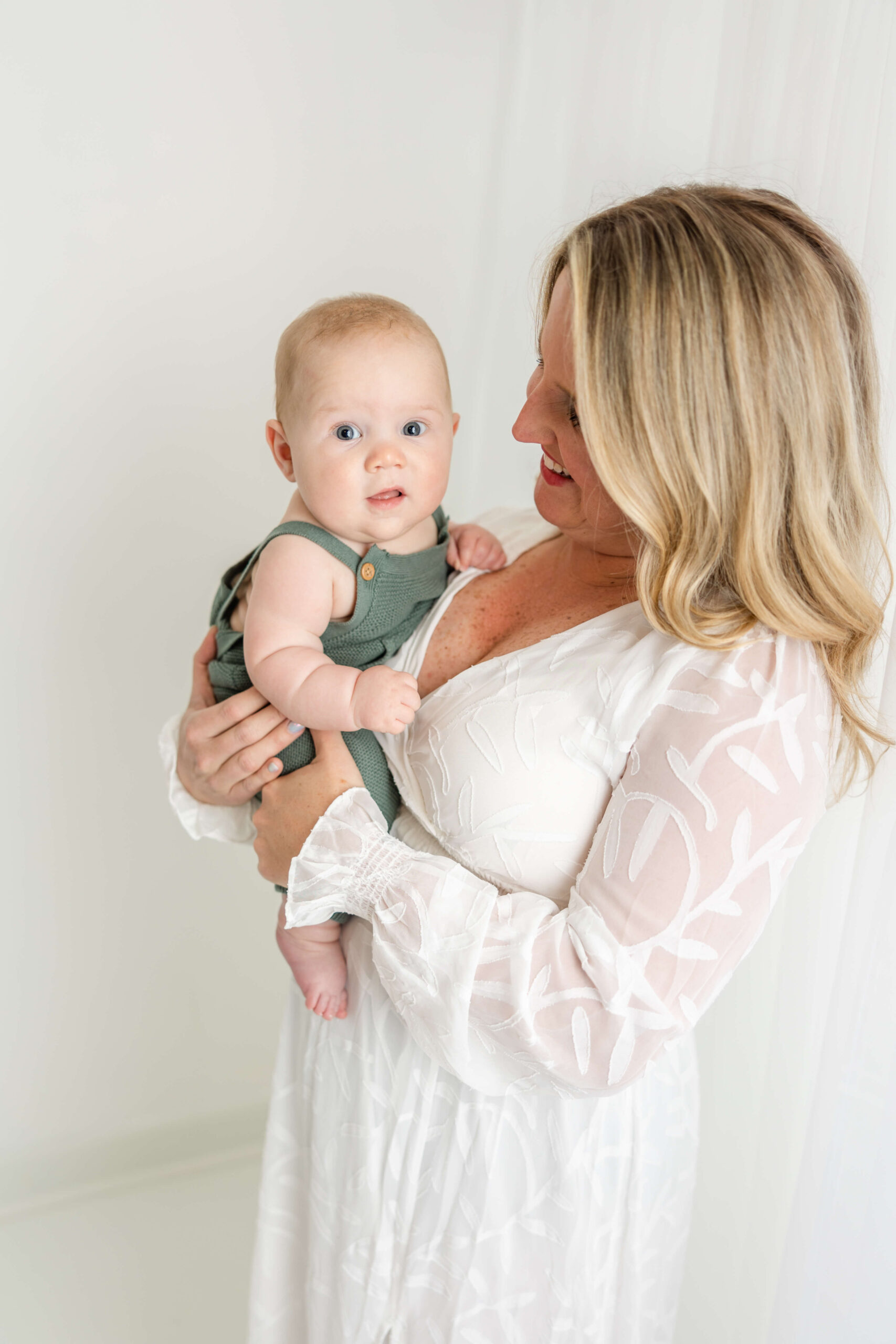 Little boy in green romper is being held by mom in a white gown, both provided by Molly Berry Photography client closet. 