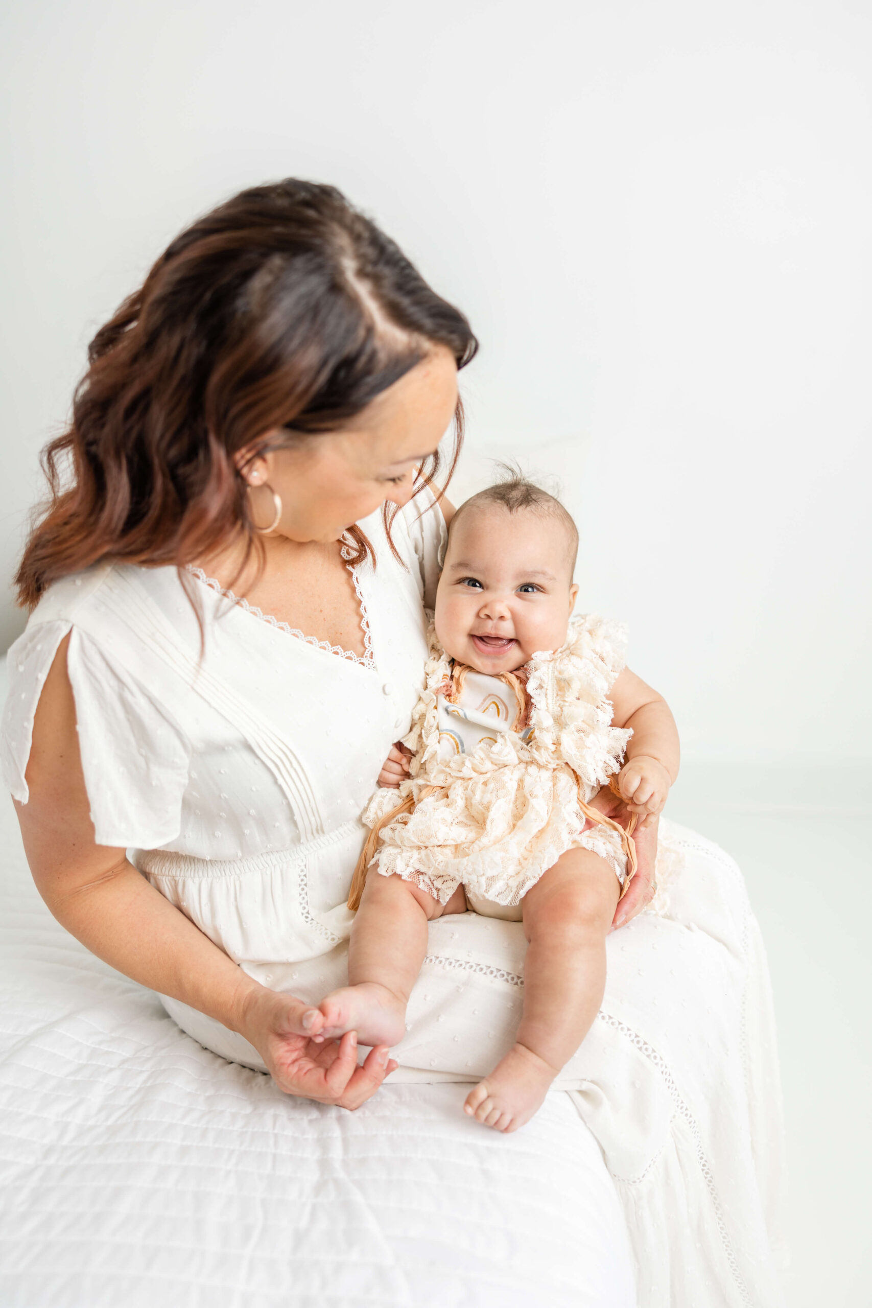Mom and her sweet girl sitting on a white bed during their motherhood session. 