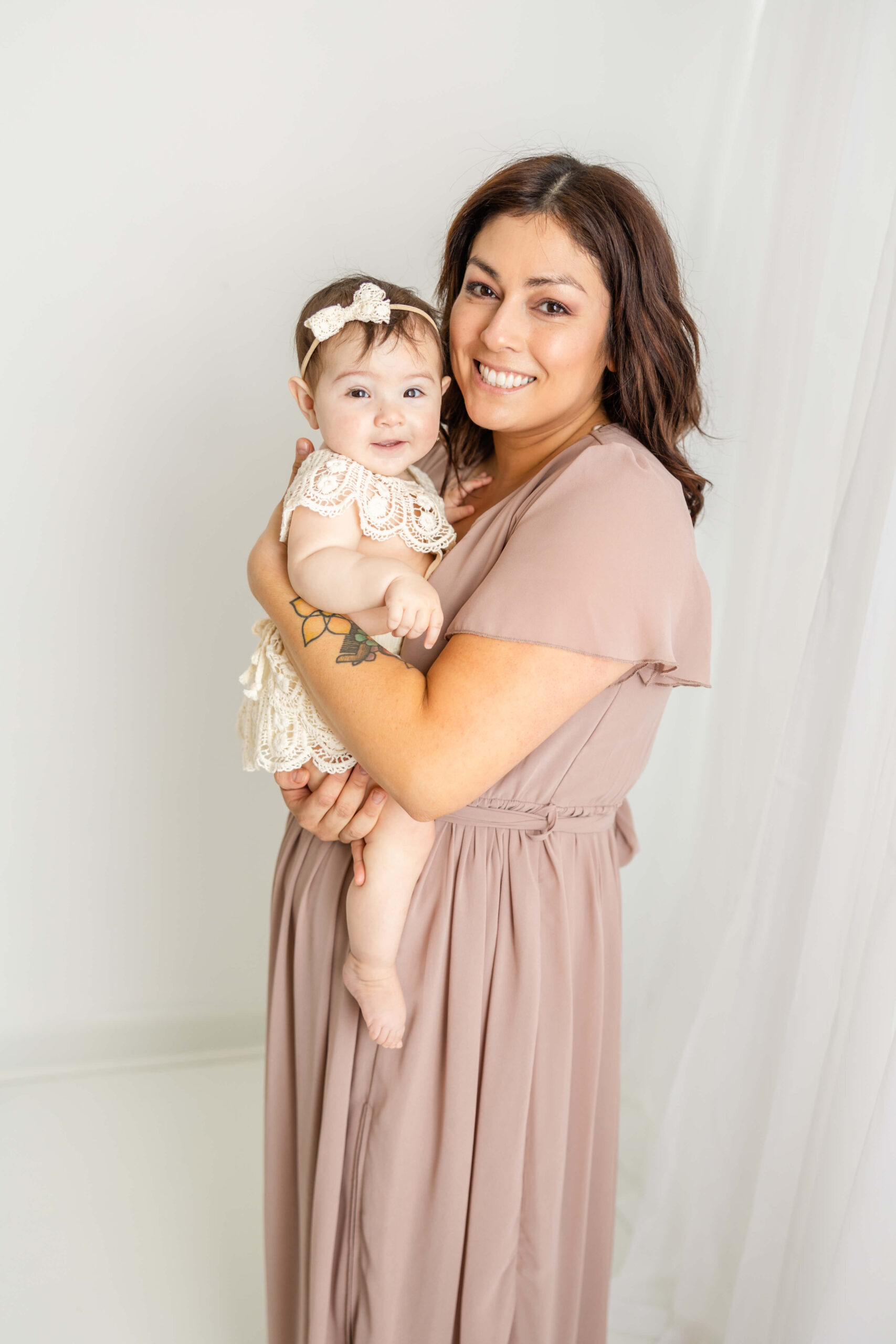 Mom in a mauve dress and her baby girl in a cream jumper, both from client closet, during their in-studio motherhood session. 