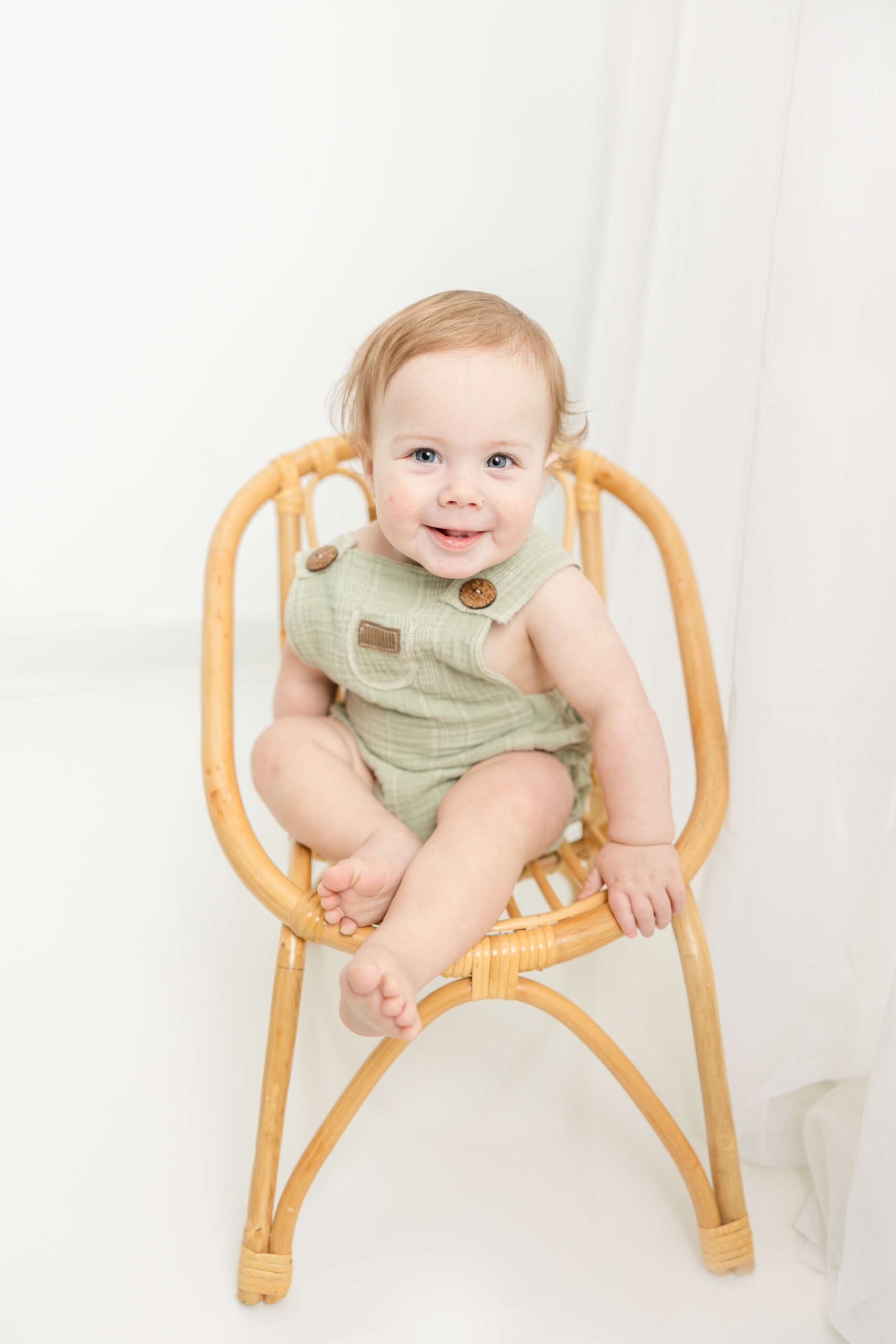 Adorable little boy in a green jumper sitting in a wicker chair during child portrait session with Molly Berry Photography.
