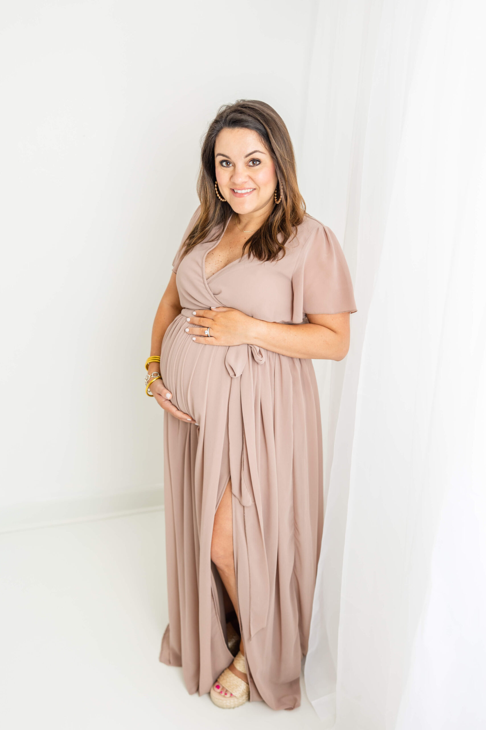 Soon to be mom wearing a full length mauve dress shows her baby bump.
