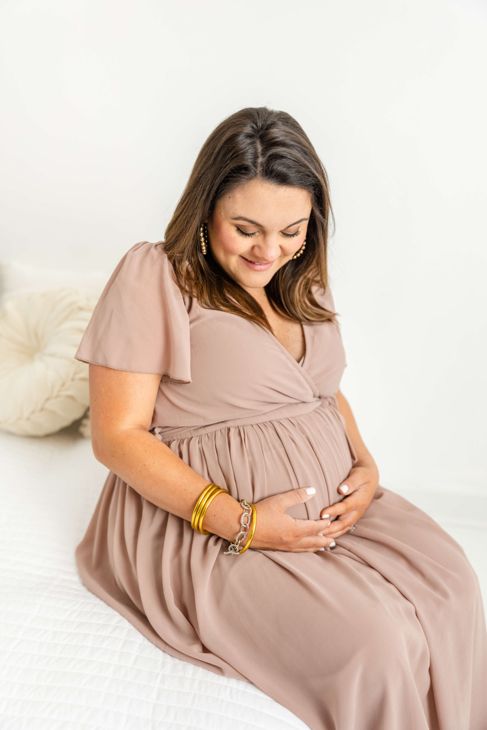 Captured pregnant mom in mauve dress sitting on a white bed.