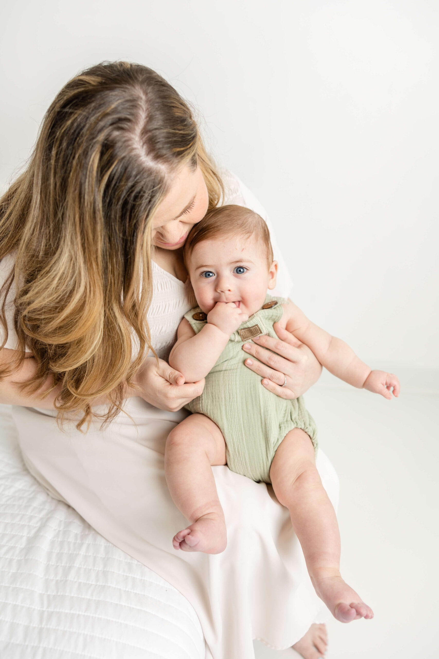 Mom hugs her baby boy, wearing a green romper, during their motherhood session. 