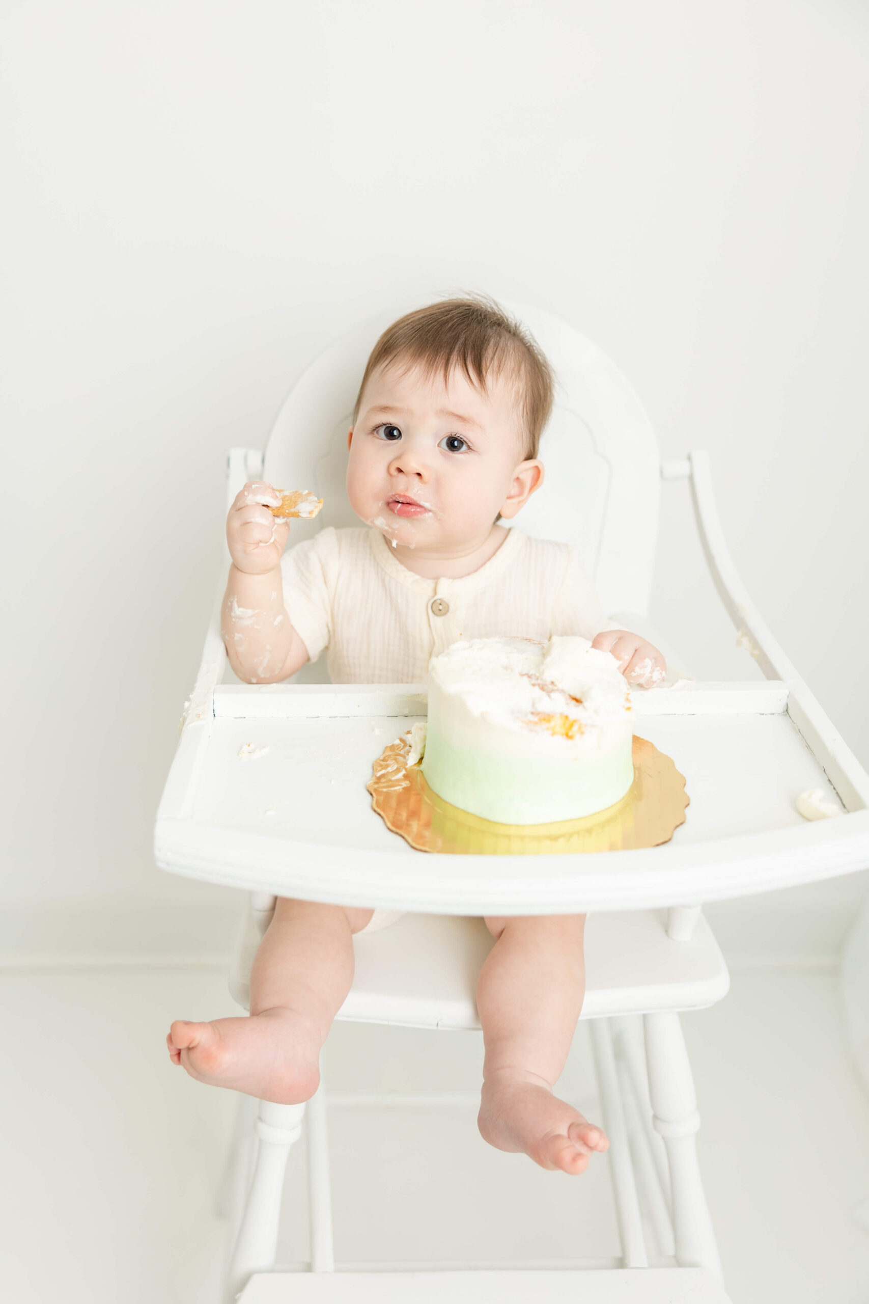 Little boy in white high chair during cake smash session. 