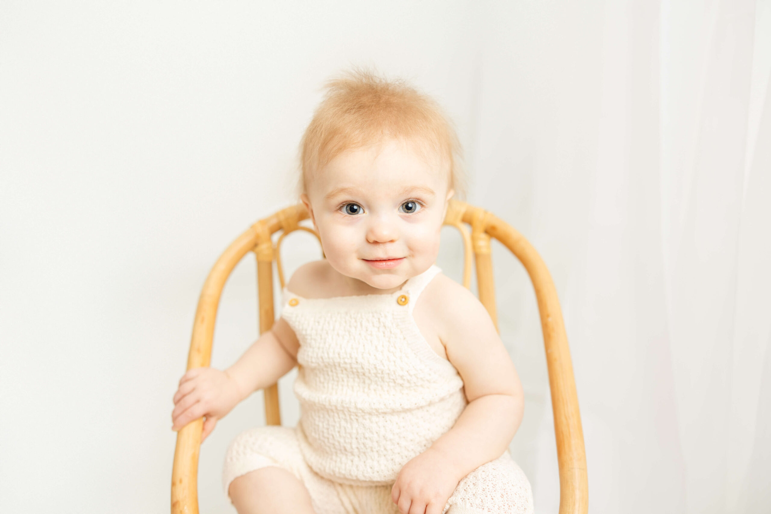 One year old sitting in a wicker chair in the studio of molly berry. 