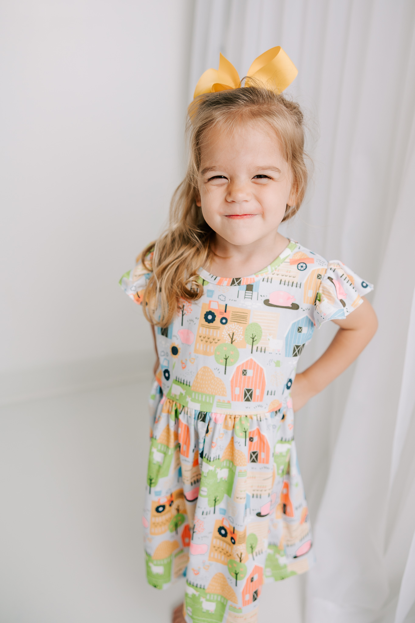 Little girl smiling during her milestone session in the studio showing off her new farm dress.