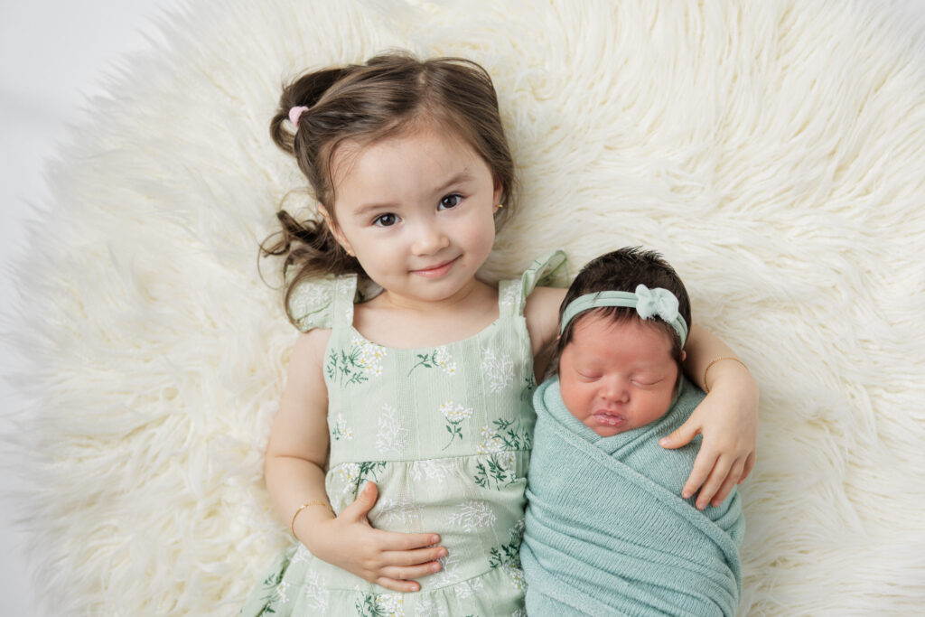 Big sister and little sister laying on the rug during their newborn session